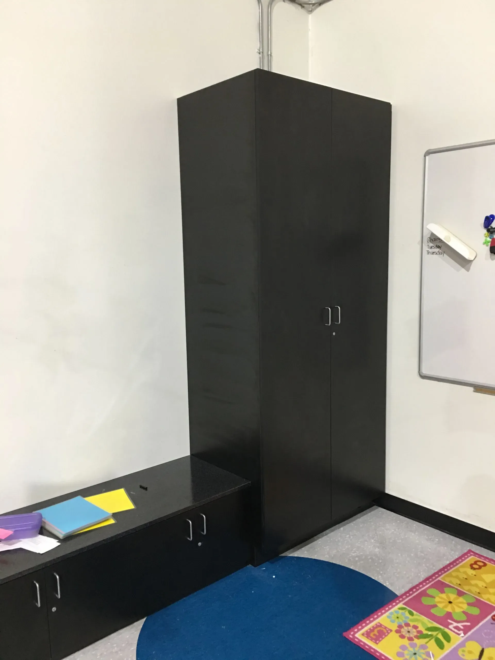 Small room with black storage cabinets, a whiteboard, and a blue rug on the floor.