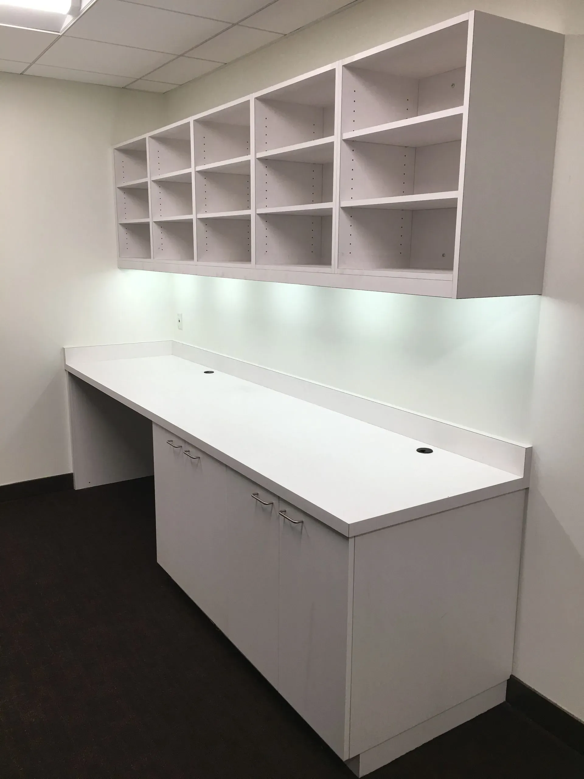 Empty office storage area with white cabinets, countertop, and wall-mounted cubby shelves