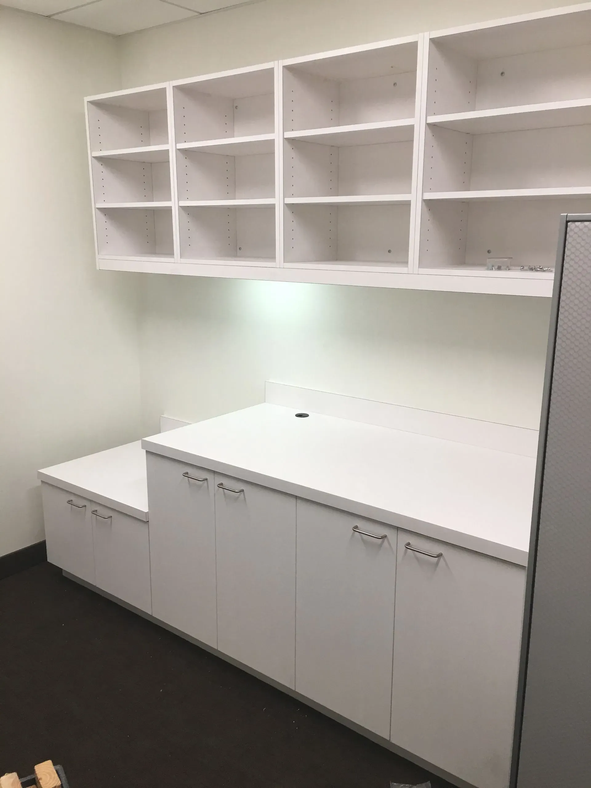 White office workspace with wall shelves, cabinets, and a countertop in a small room