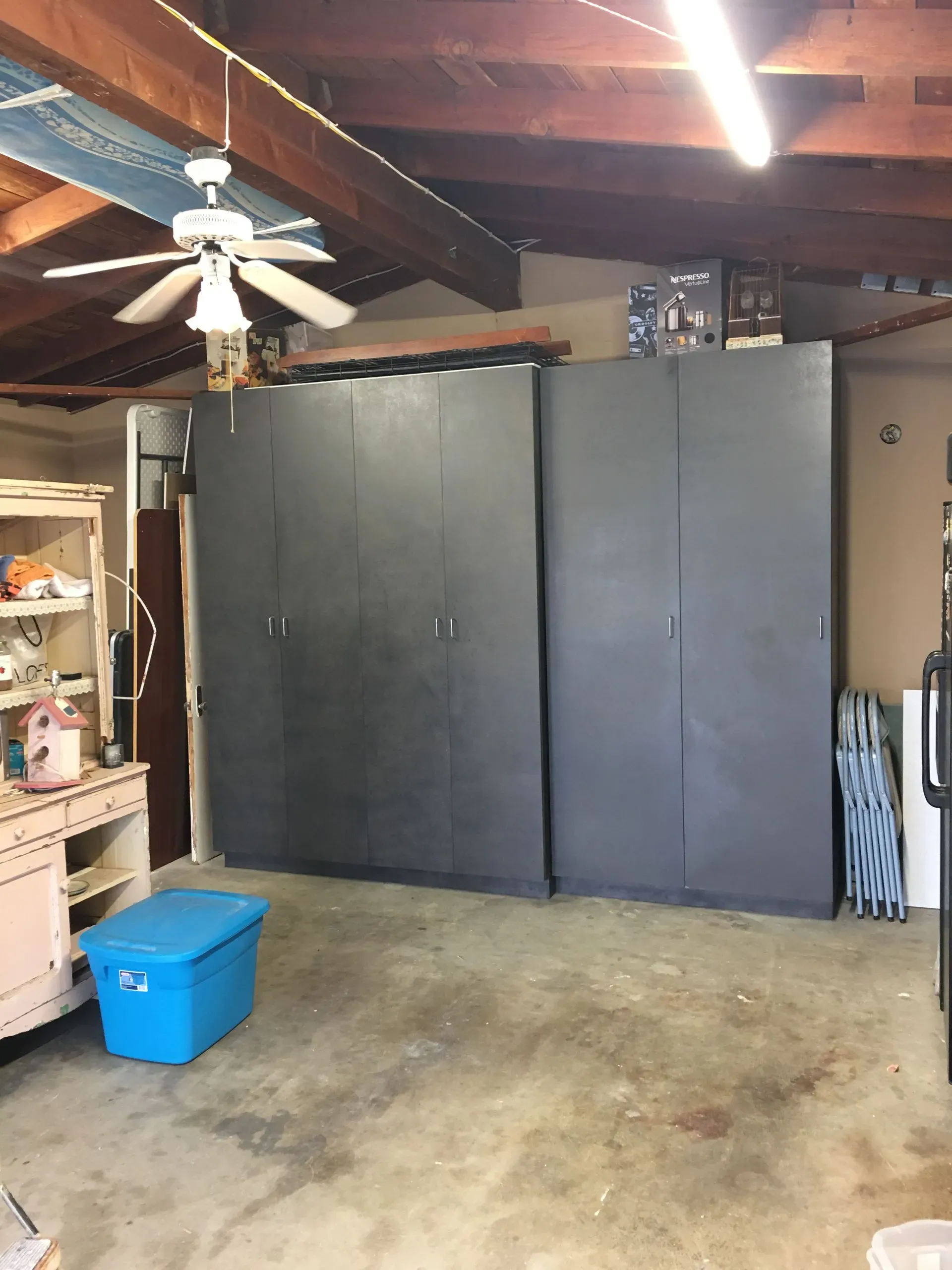 Basement garage with large gray cabinet doors, ceiling fan, shelves, and a blue storage bin on the floor