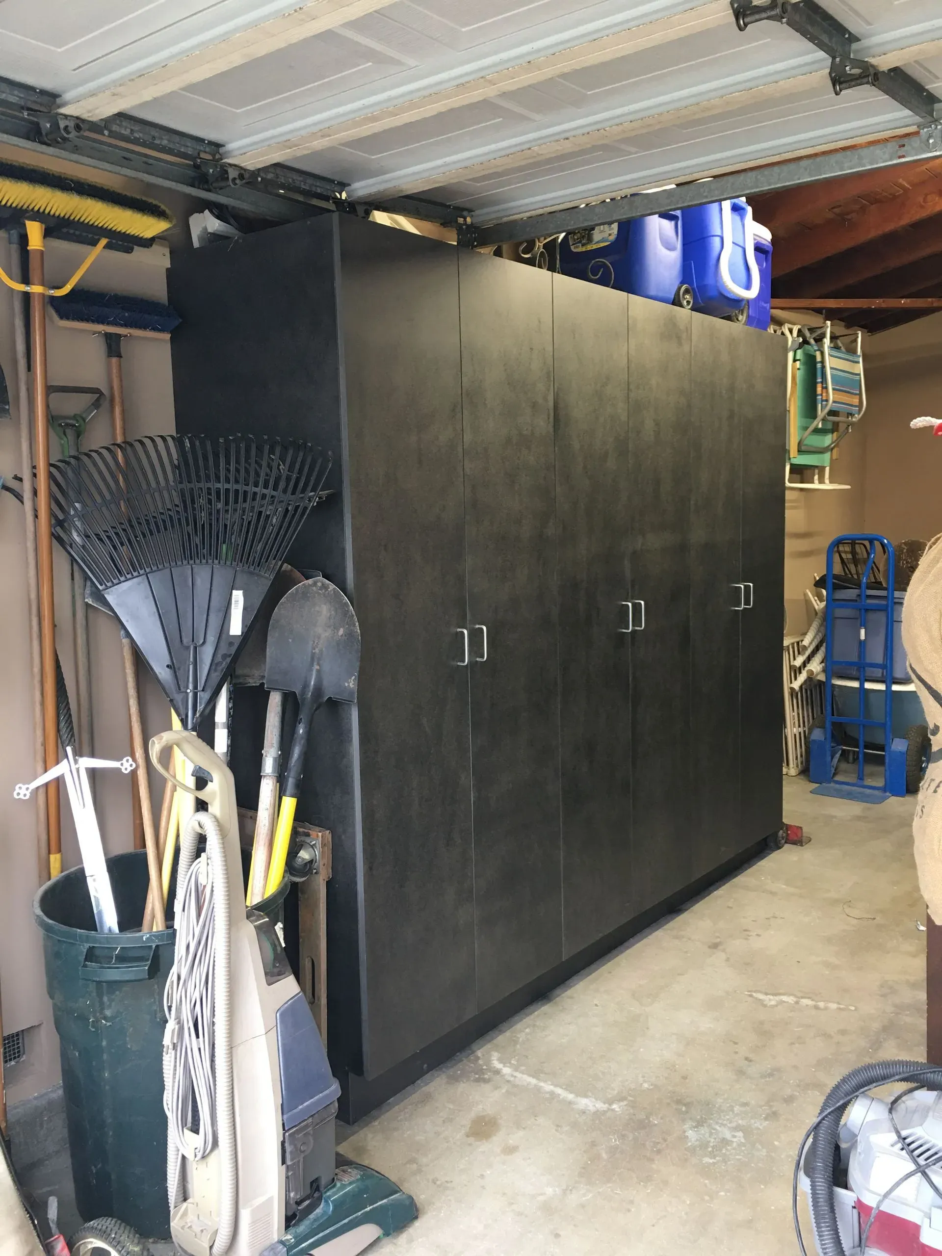 Garage storage area with a large black cabinet, tools, and sports equipment stacked along the walls.