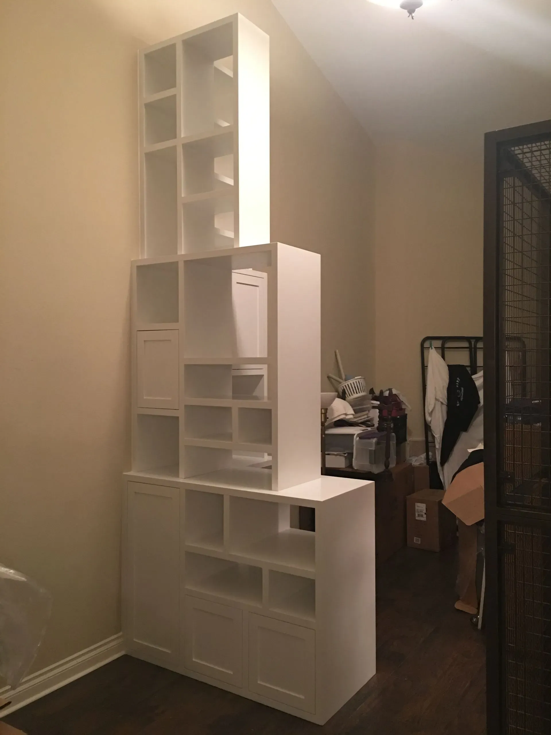 Tall white shelving unit with cubbies in a beige room, near a doorway and clothes rack.