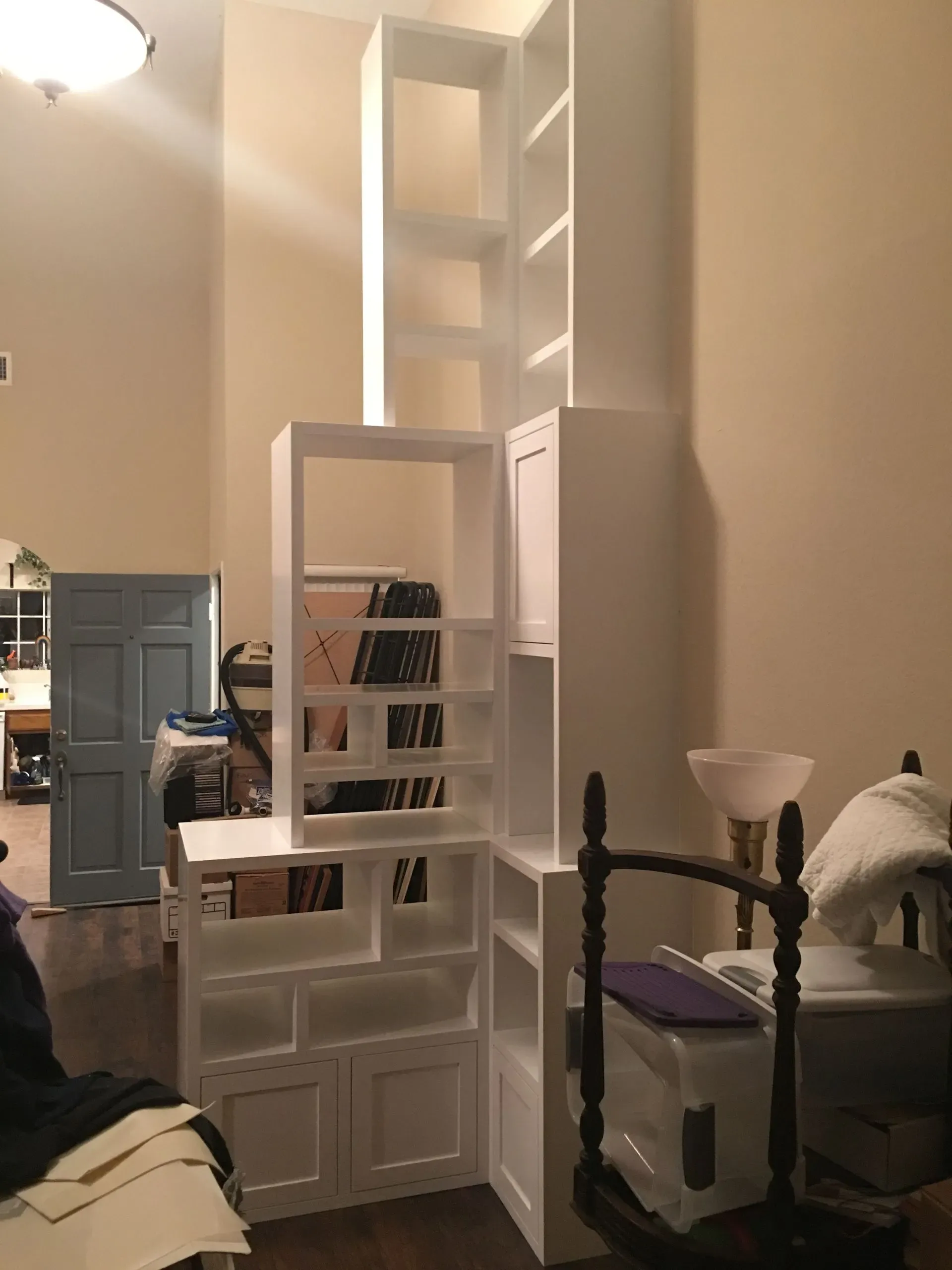 Tall white bookshelf with mirrored inset in a beige living room beside a black metal bed frame and white lamp.