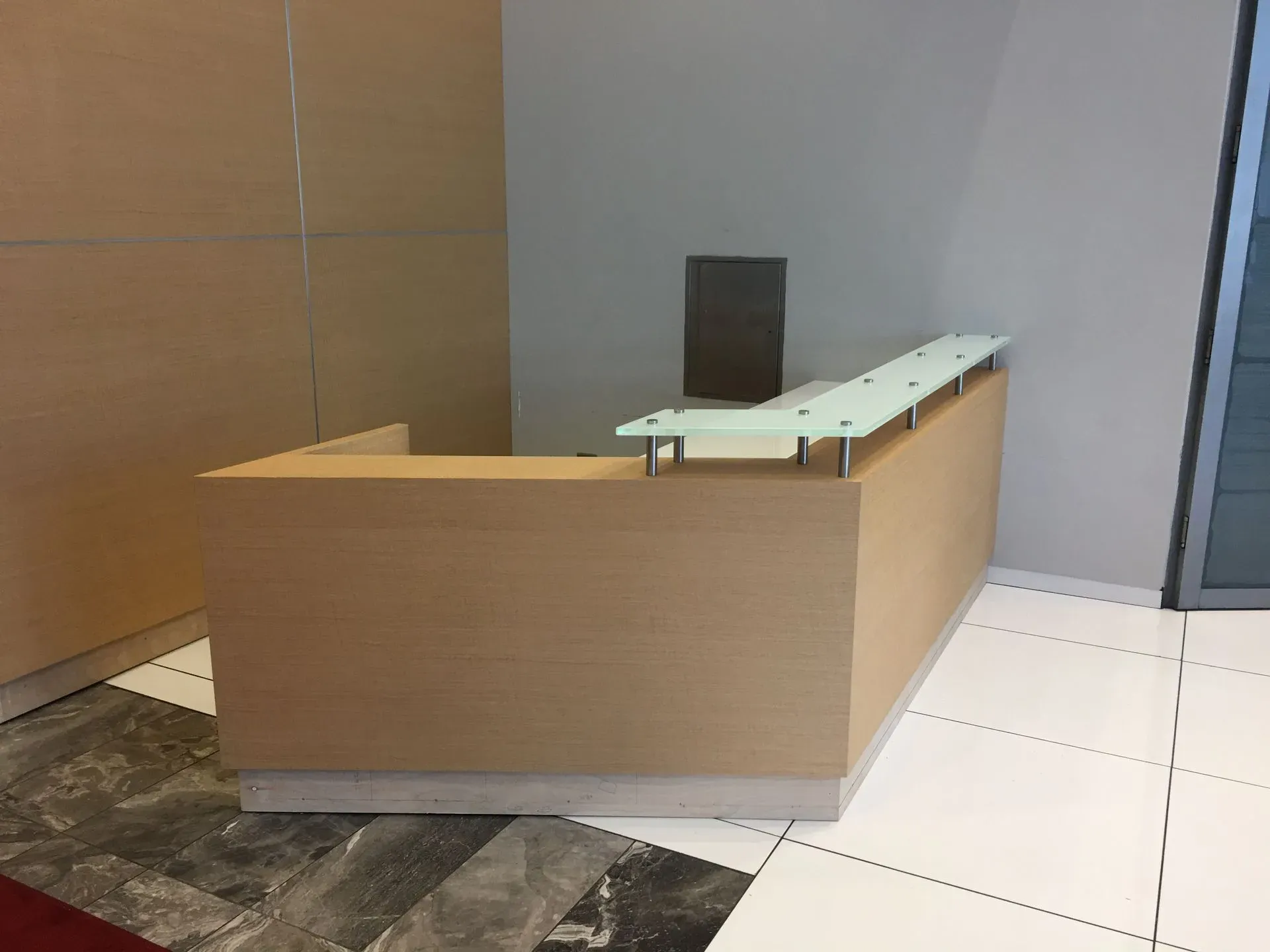 Empty reception desk in a modern office lobby with wood paneling and tiled floor
