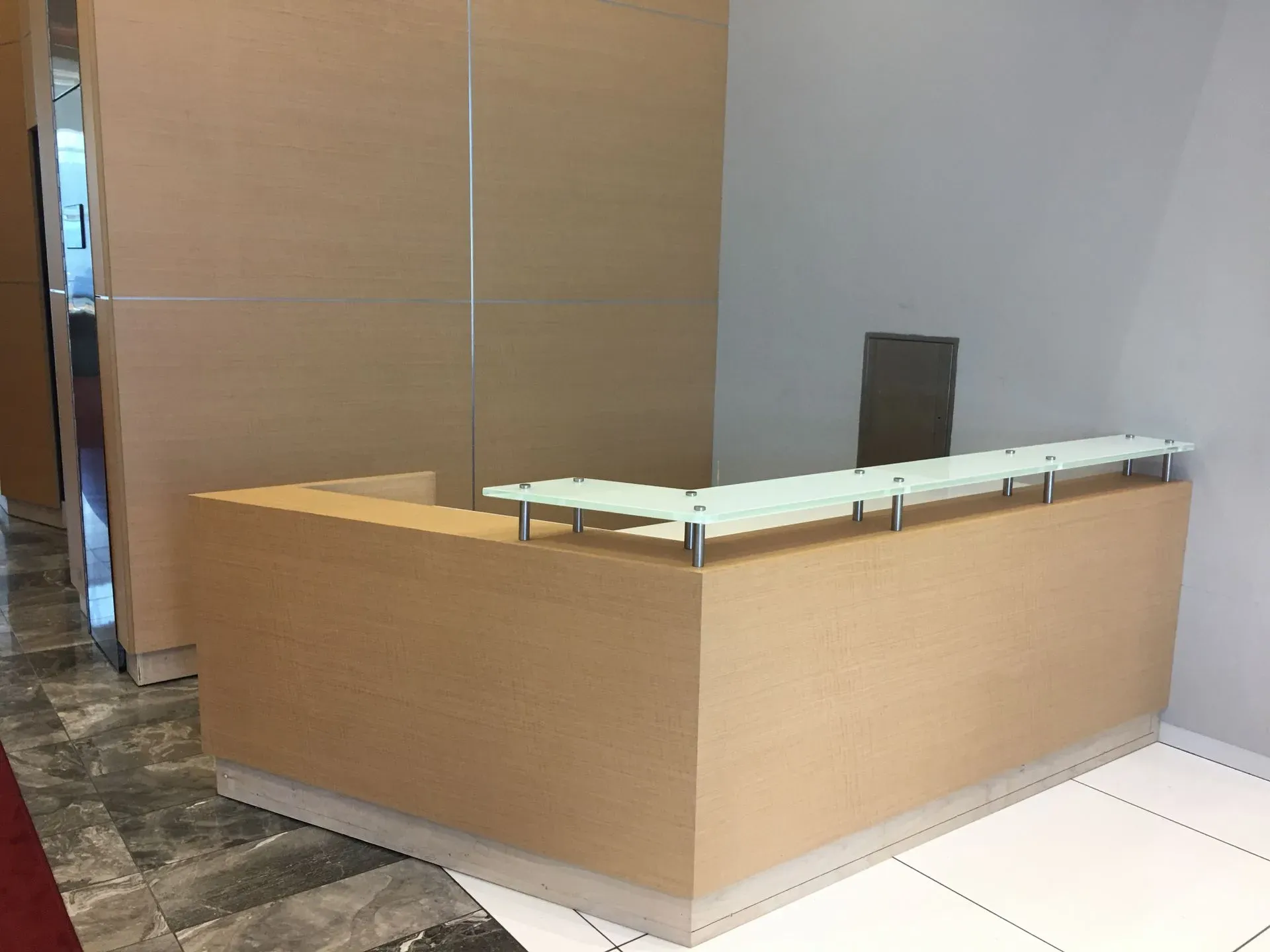 Modern lobby reception desk with light wood panels and glass top on tiled floor