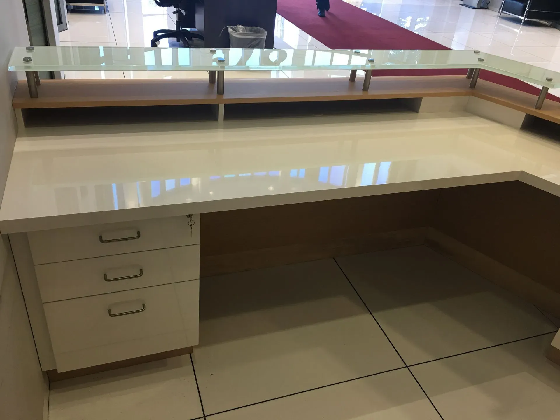 Empty reception desk with drawers, beige counter, and glass shelf in a tiled lobby