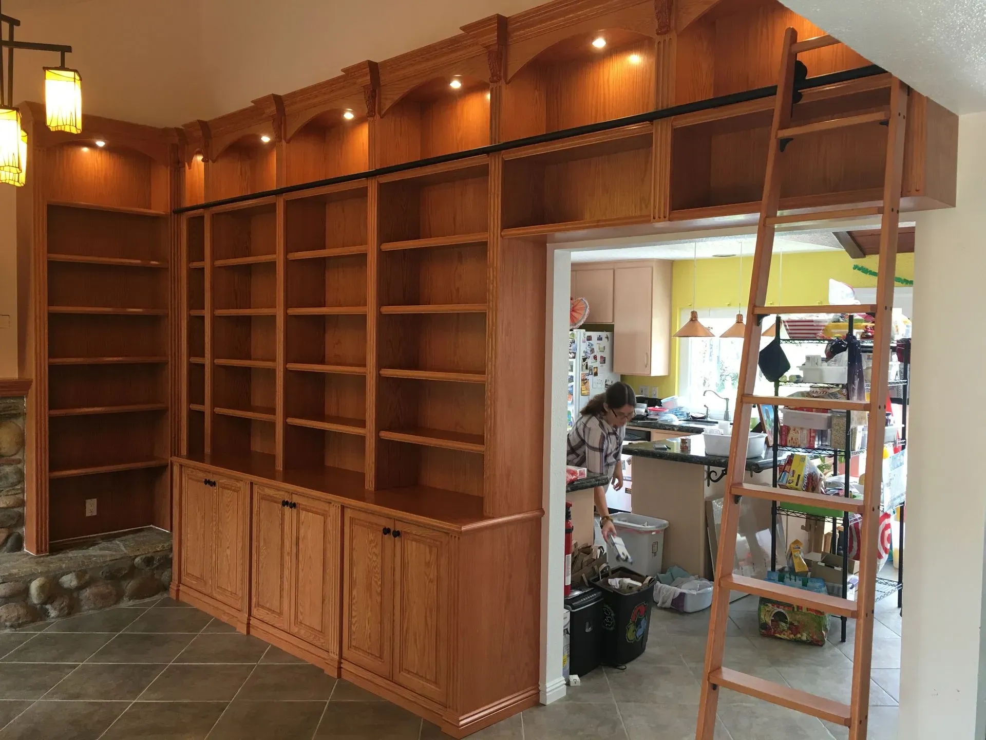 Wood-paneled built-in shelving and cabinets in a room, with an open doorway to a cluttered kitchen area.