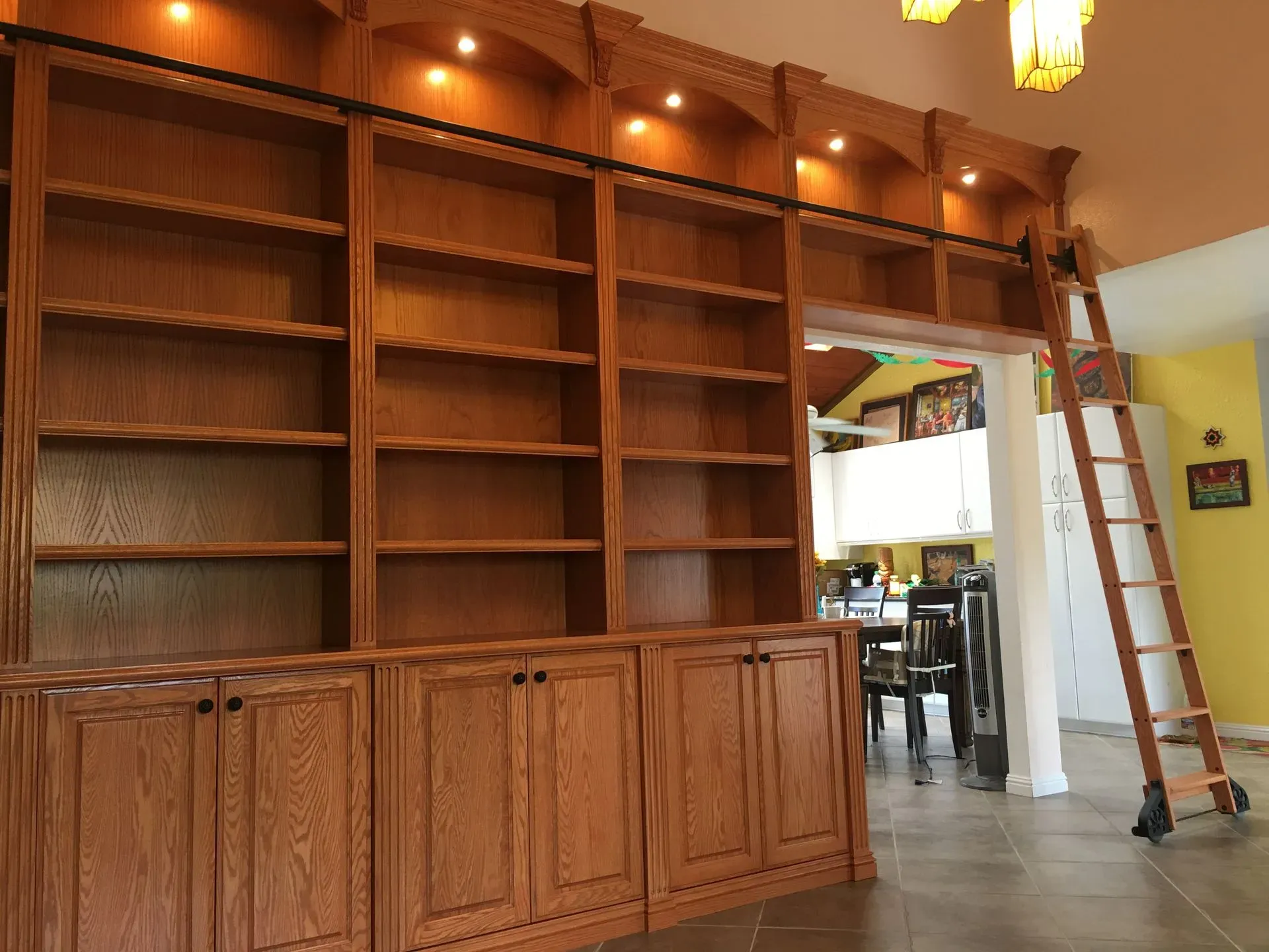 Large wooden built-in shelves and cabinets in a room, with a ladder beside an open doorway.