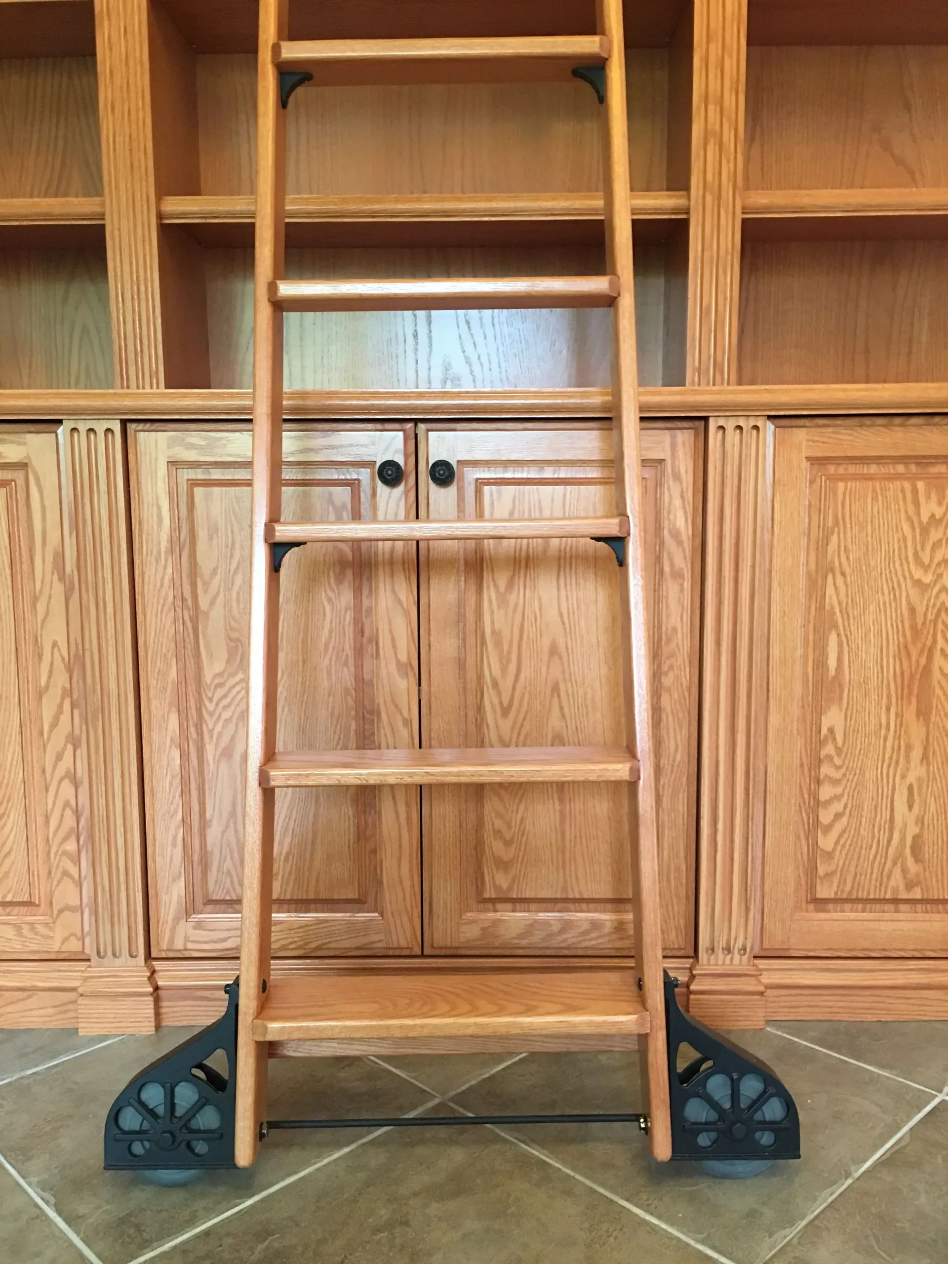 Wooden step ladder centered in front of built-in cabinets with black corner supports.