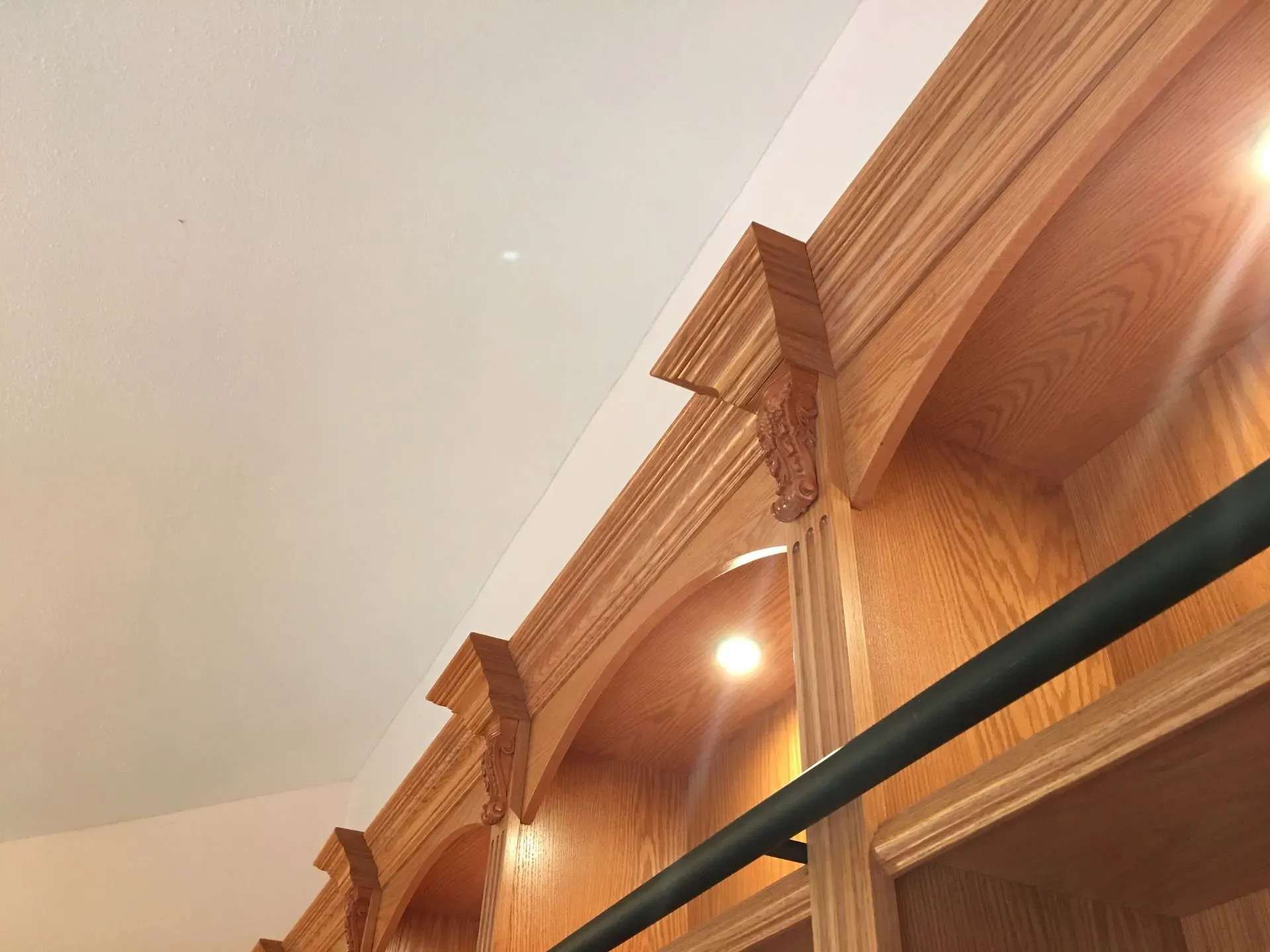 Wooden kitchen cabinets with crown molding, recessed lights, and a black metal rod against a light ceiling