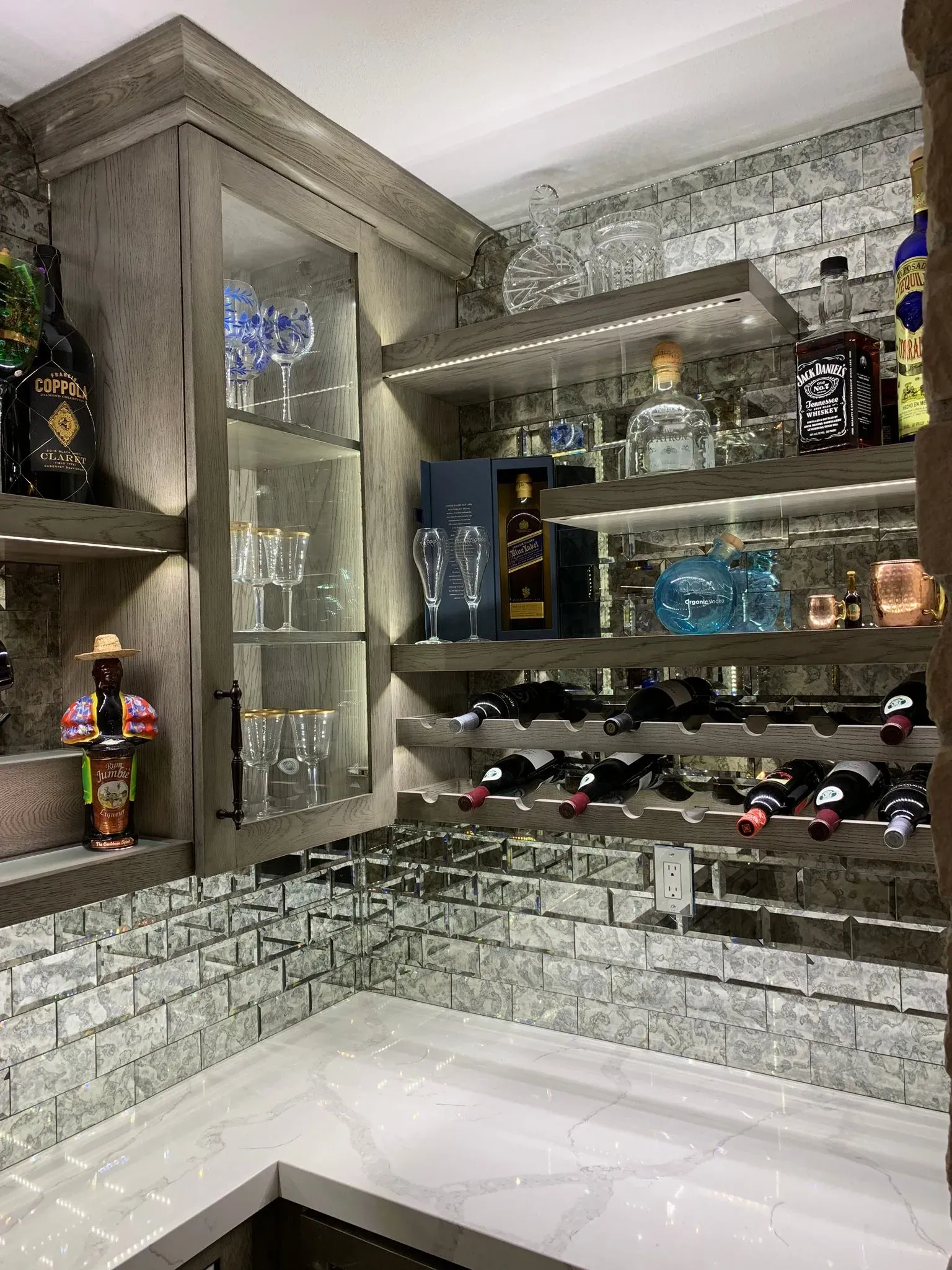 Modern kitchen corner with gray cabinets, mirrored backsplash, wine rack, and white countertop.