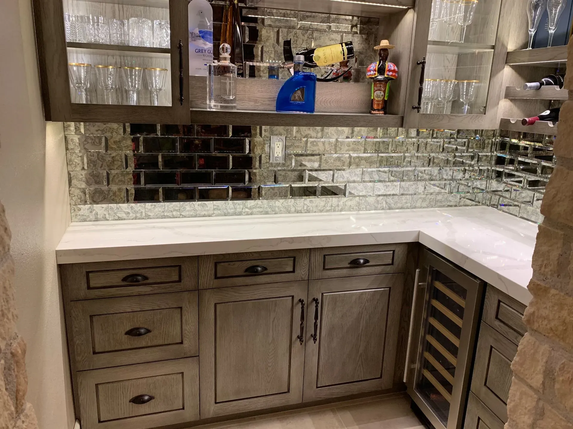Modern kitchen bar with mirrored tile backsplash, white countertop, and wood cabinets with wine rack