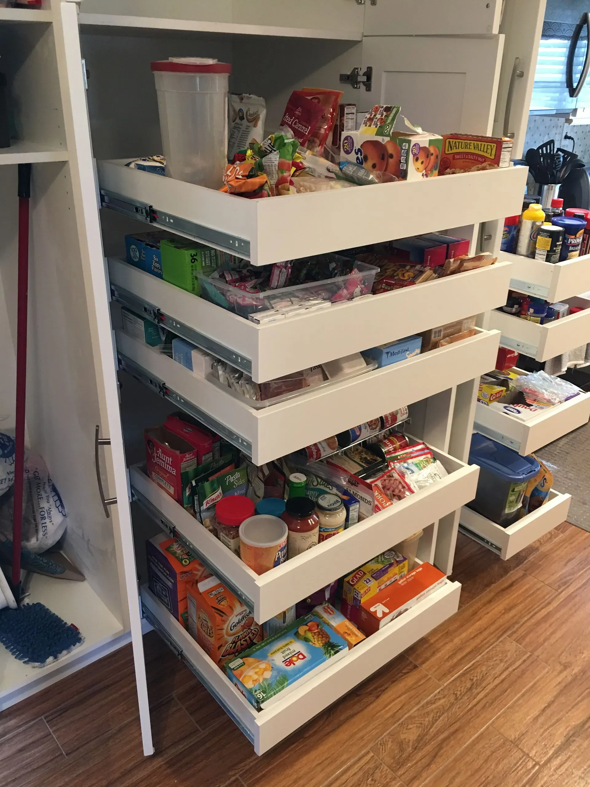 White rolling storage cart filled with assorted snacks and small items in a pantry or closet.