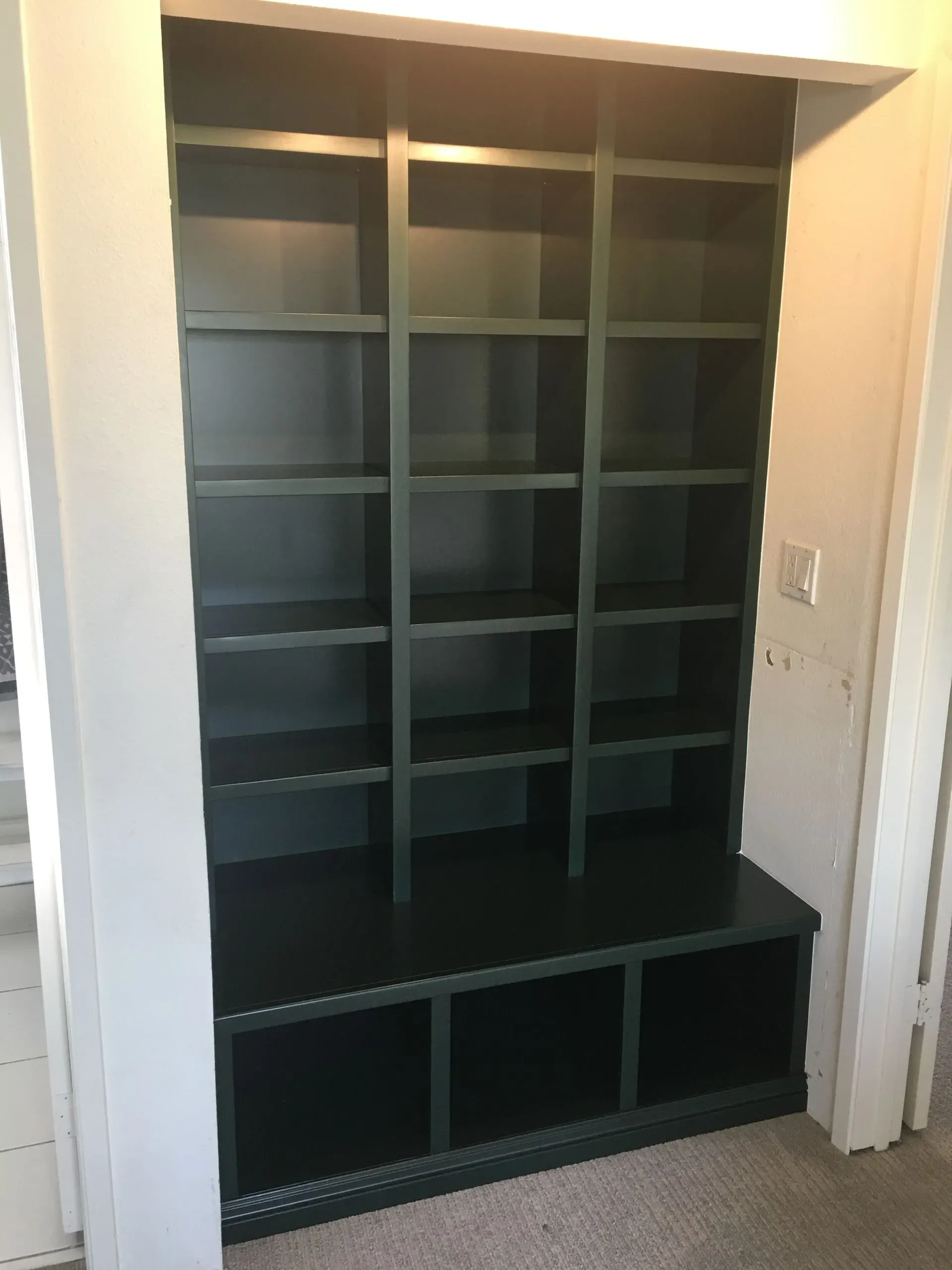 Black cubby shelf unit with open compartments in a doorway, with a dark bench/storage base.