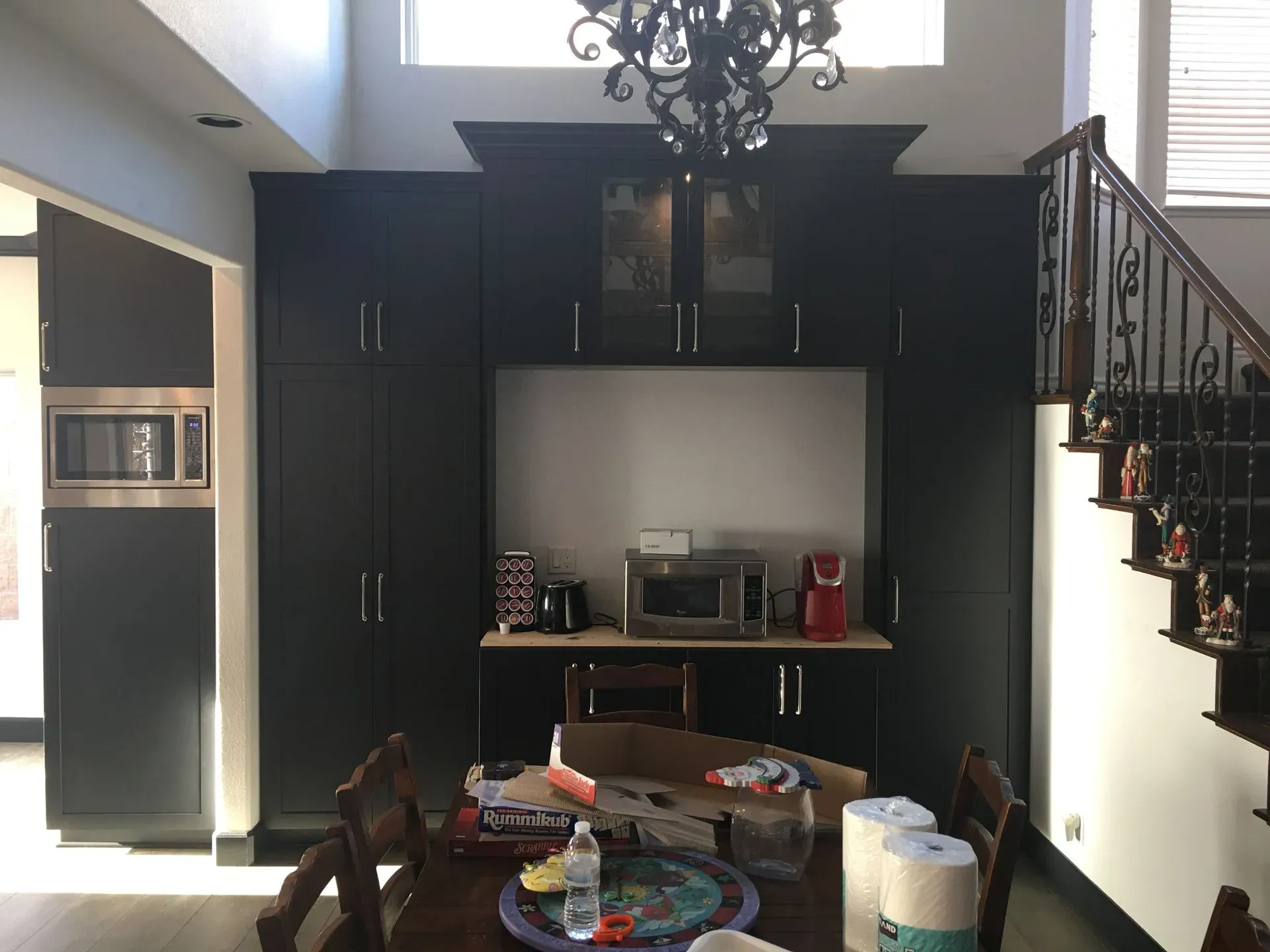 Living room with dark built-in cabinets, chandelier, staircase, and a cluttered dining table in the foreground