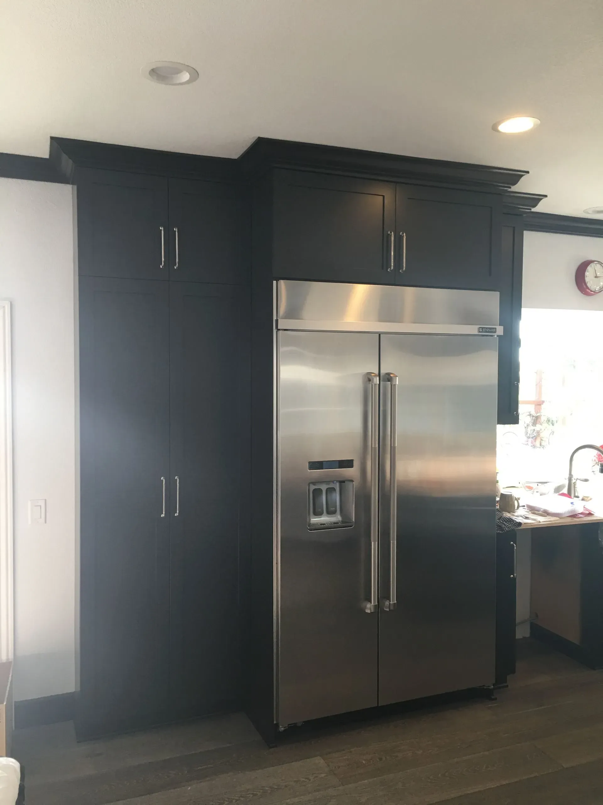Kitchen with stainless steel refrigerator between tall black cabinets and a doorway to the right