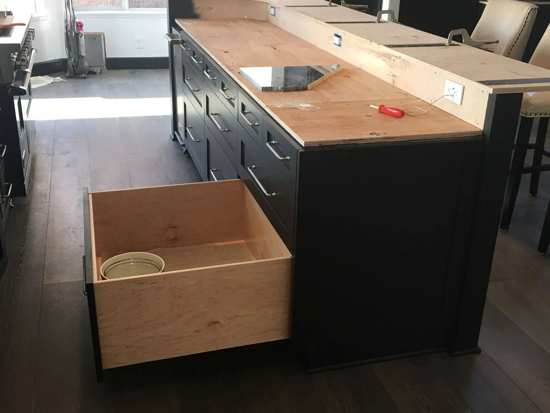Kitchen island with open drawer, black cabinets, and a wood countertop in a bright room