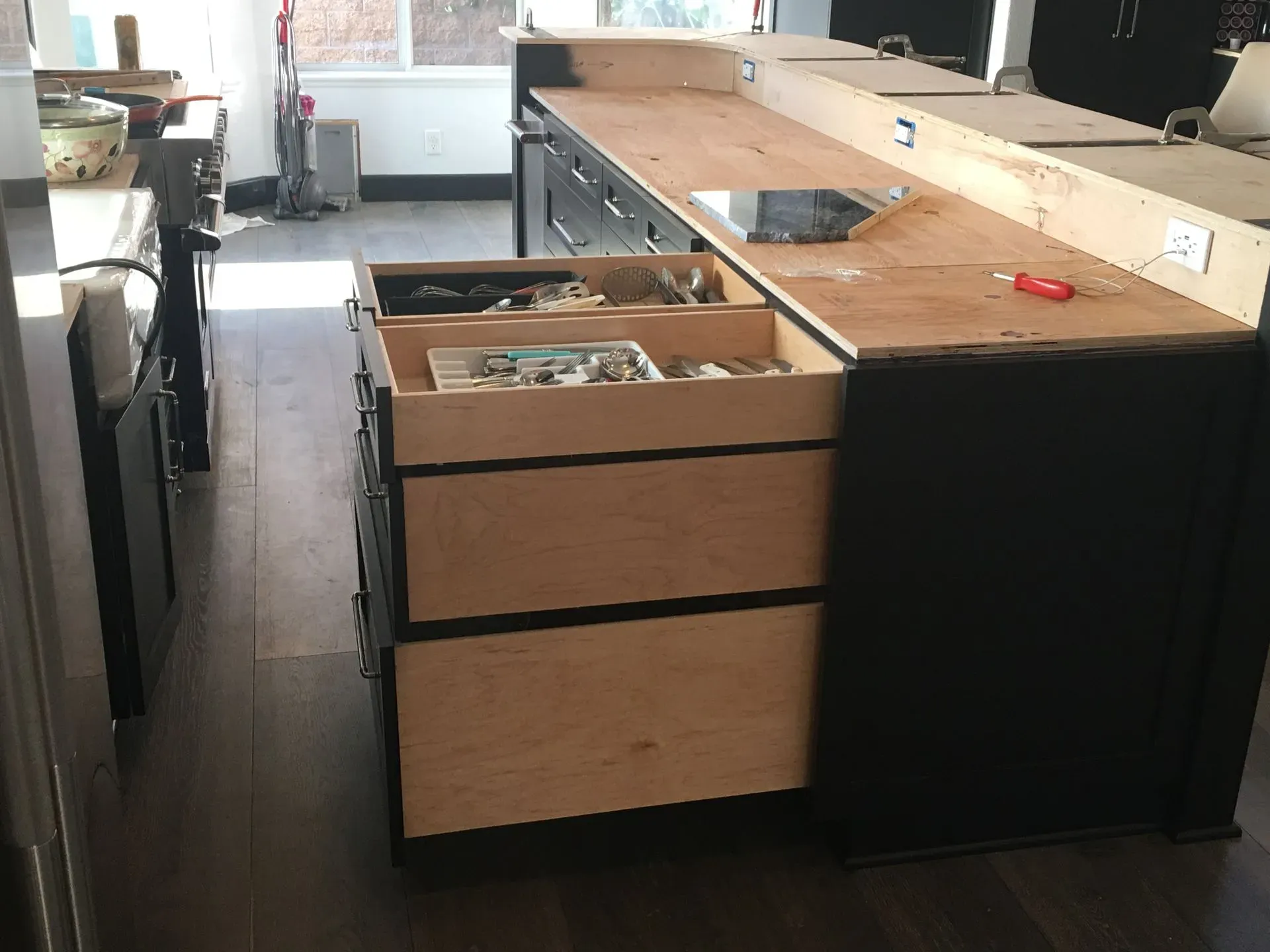Modern kitchen with open drawers, black island, and light wood countertops in a bright room