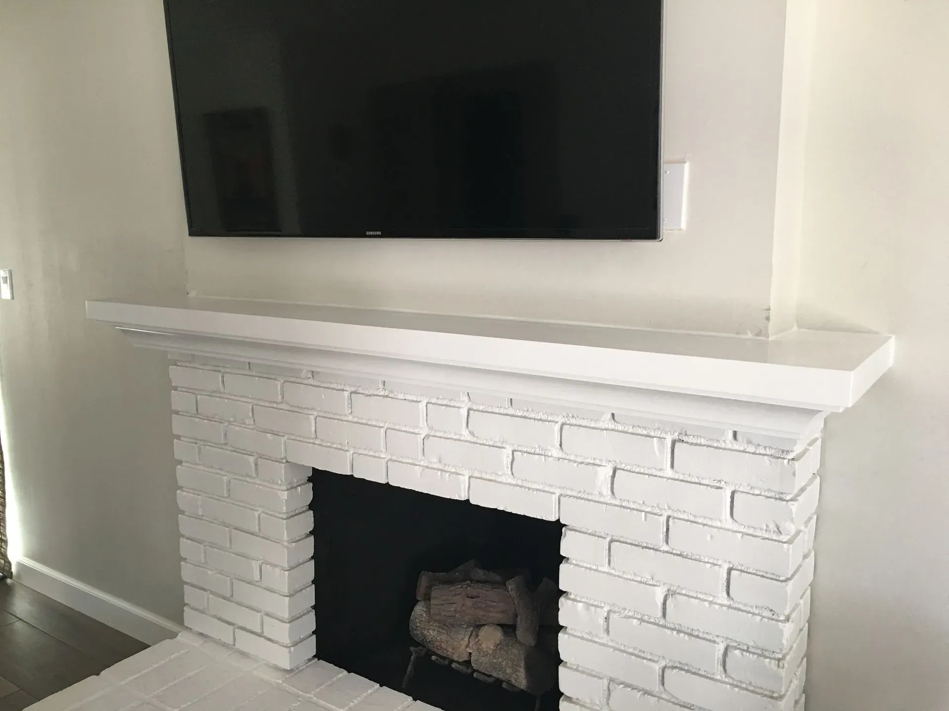 White painted brick fireplace with a mantel under a wall-mounted TV in a living room