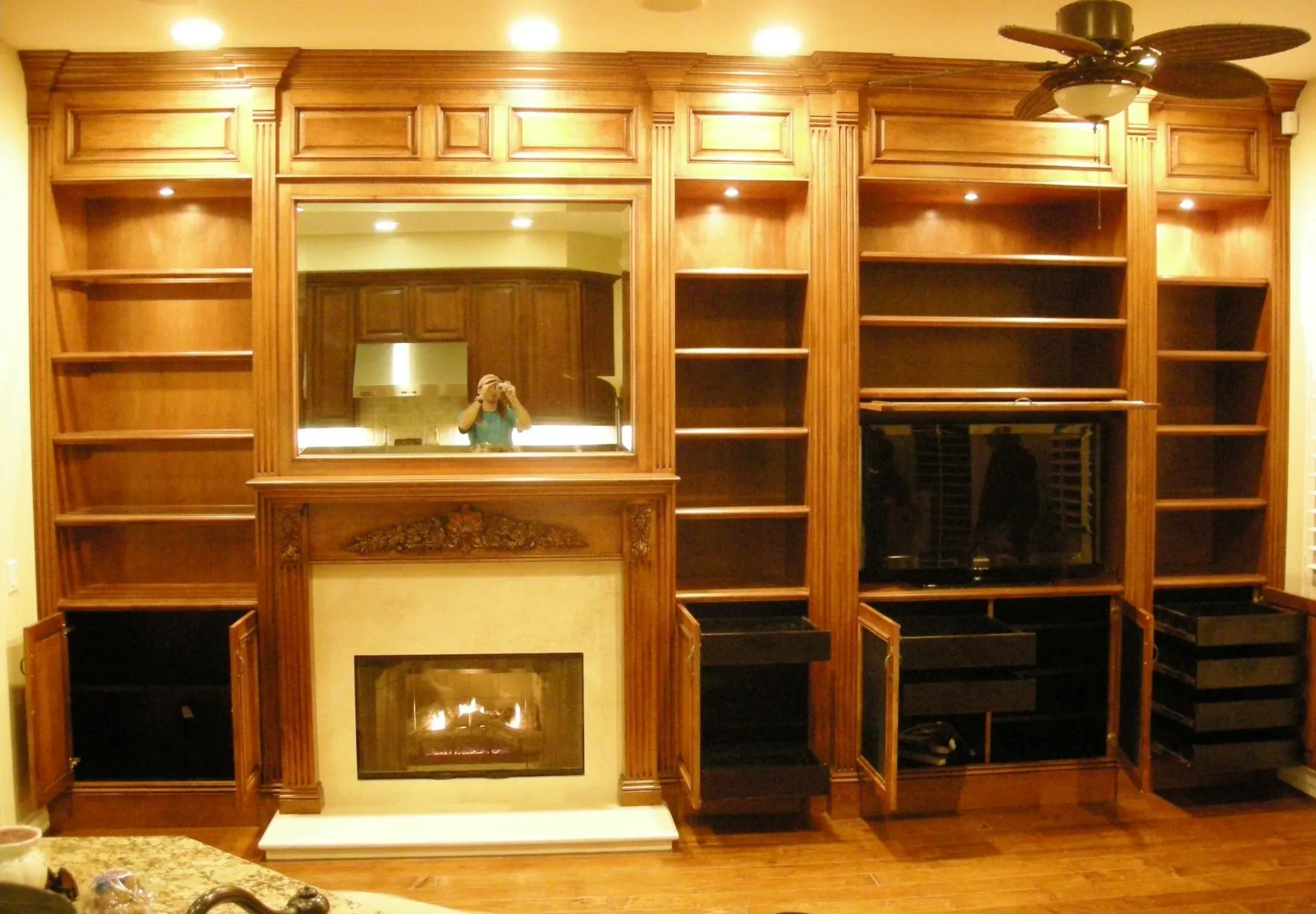 Built-in wooden entertainment center with shelves, mirror, fireplace, and TV in a warm living room