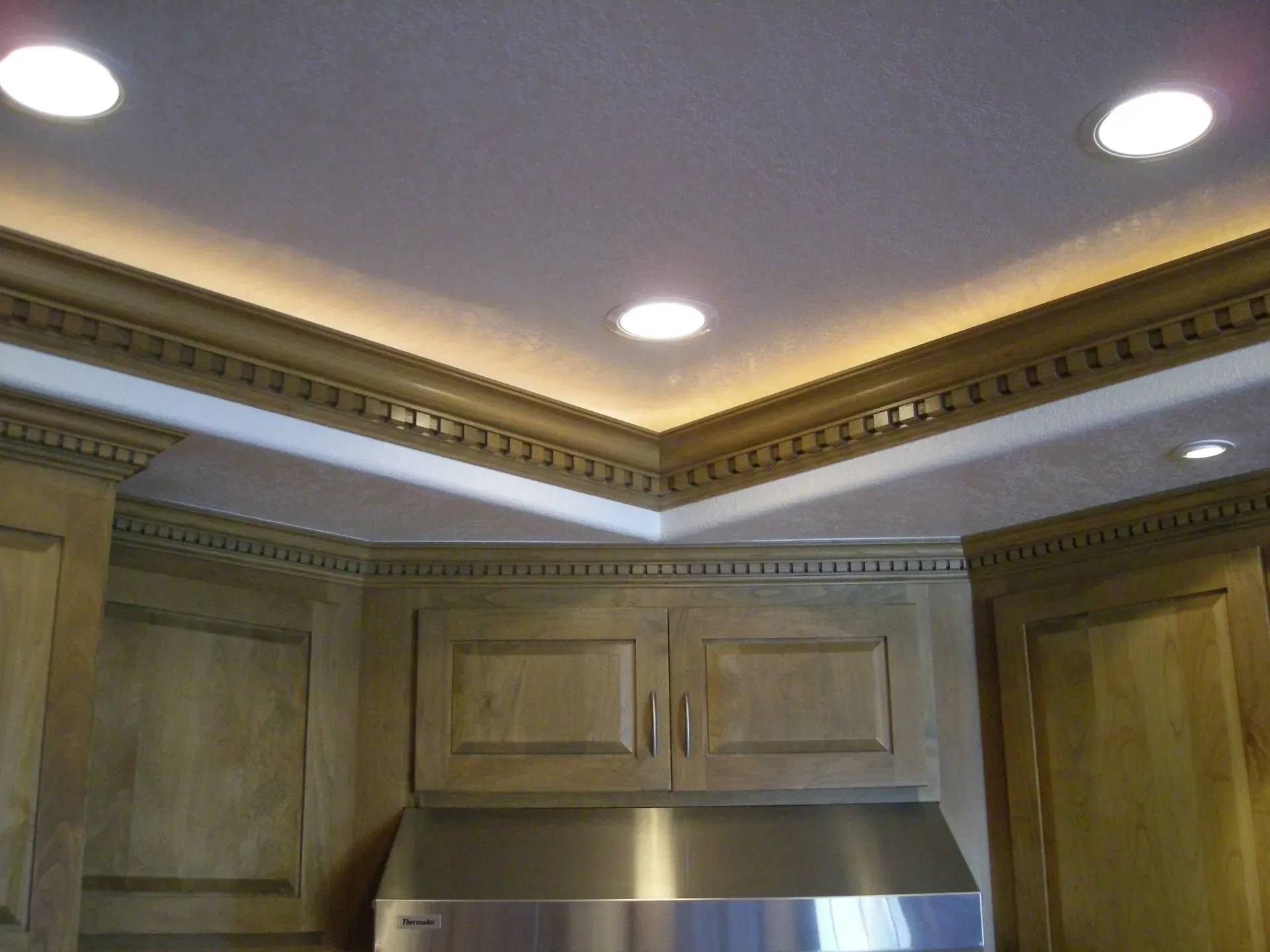 Kitchen ceiling with recessed lights and decorative crown molding above wood cabinets