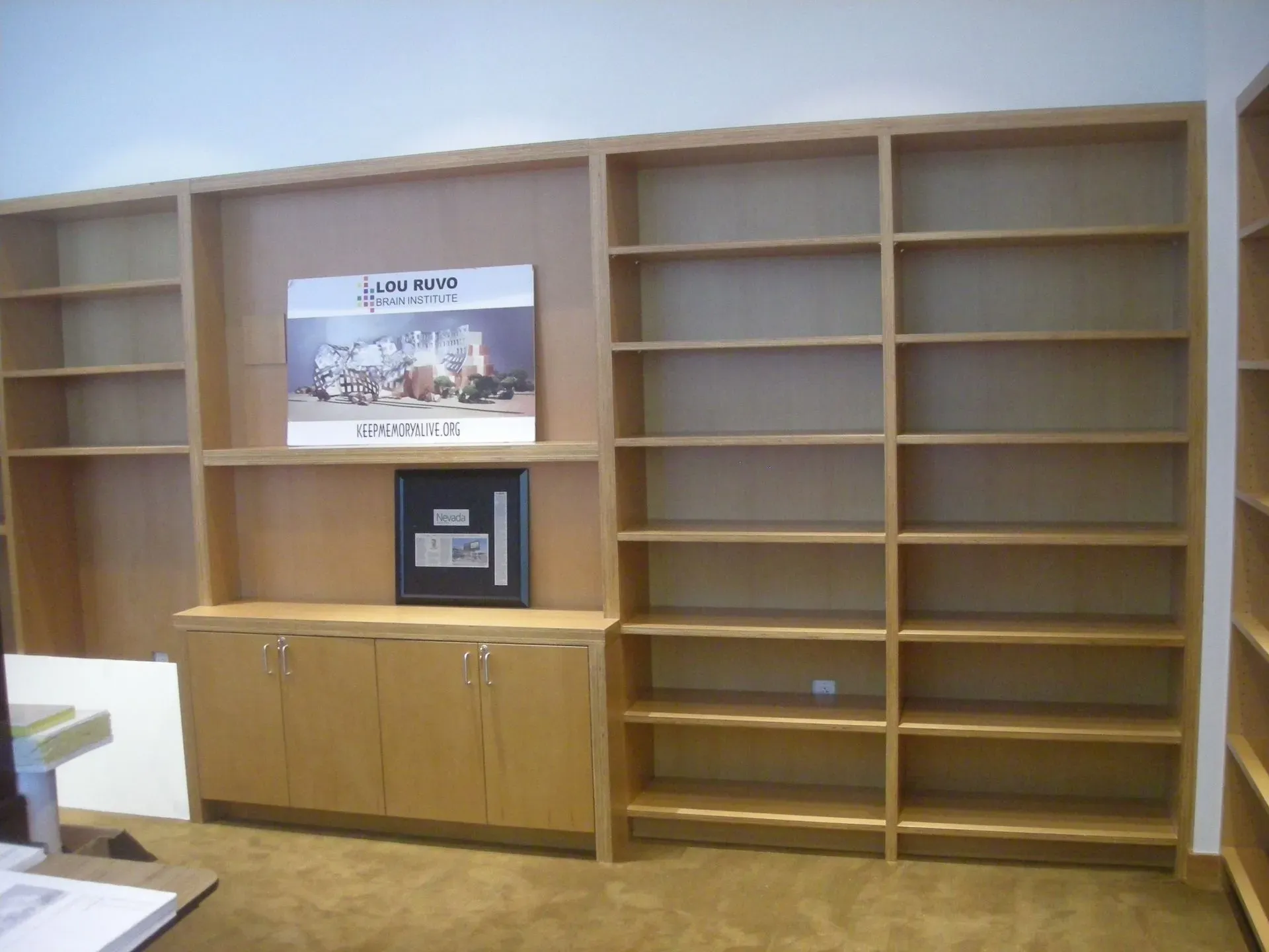 Empty wooden bookshelves with a cabinet and framed sign in the center of a room
