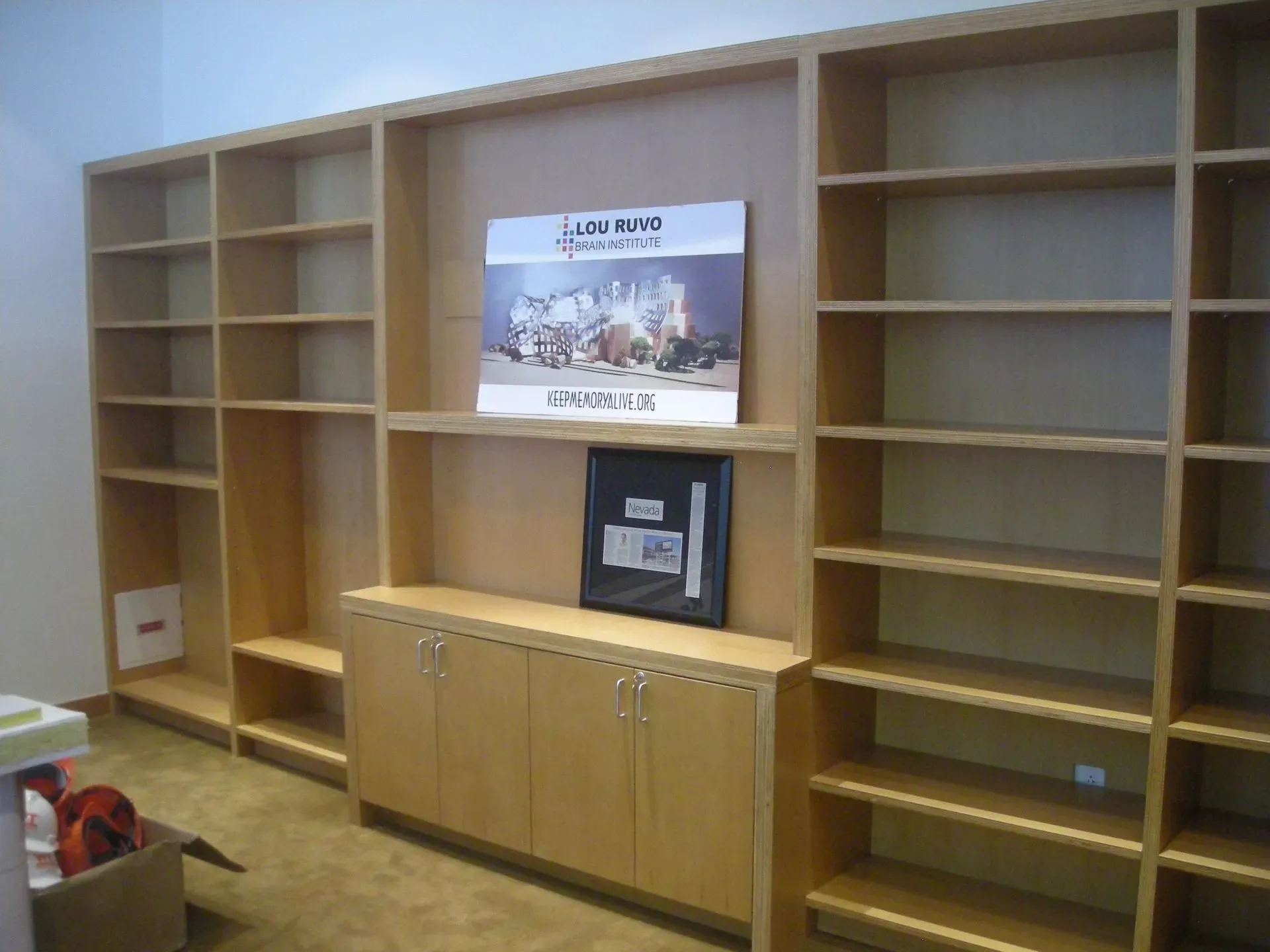 Empty office wall with built-in wooden bookshelves, a cabinet, and a wall-mounted sign above it