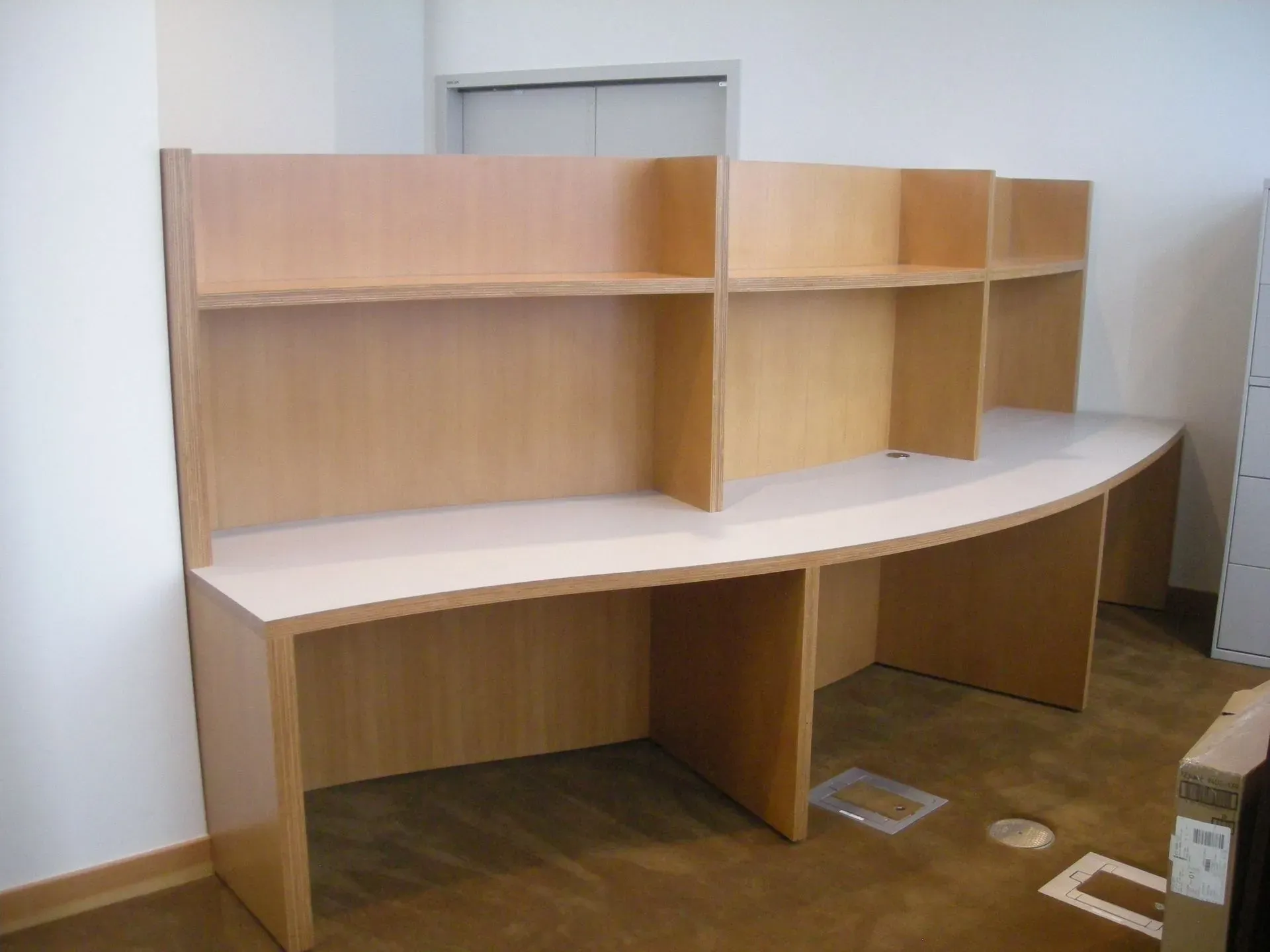 Curved wooden office desk with shelves and partitions against a wall in an empty room