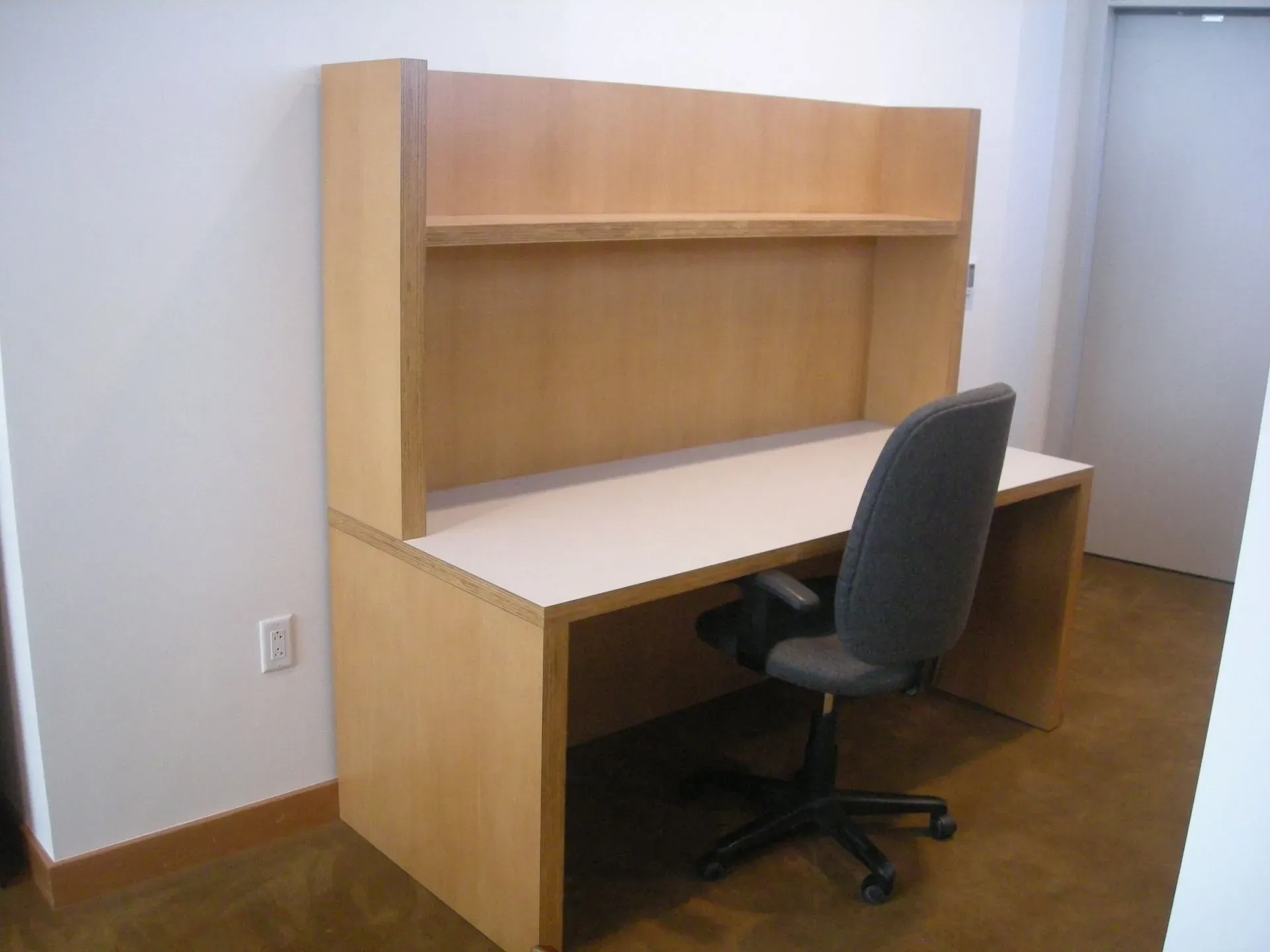 Wooden desk with hutch and black office chair in a sparse room