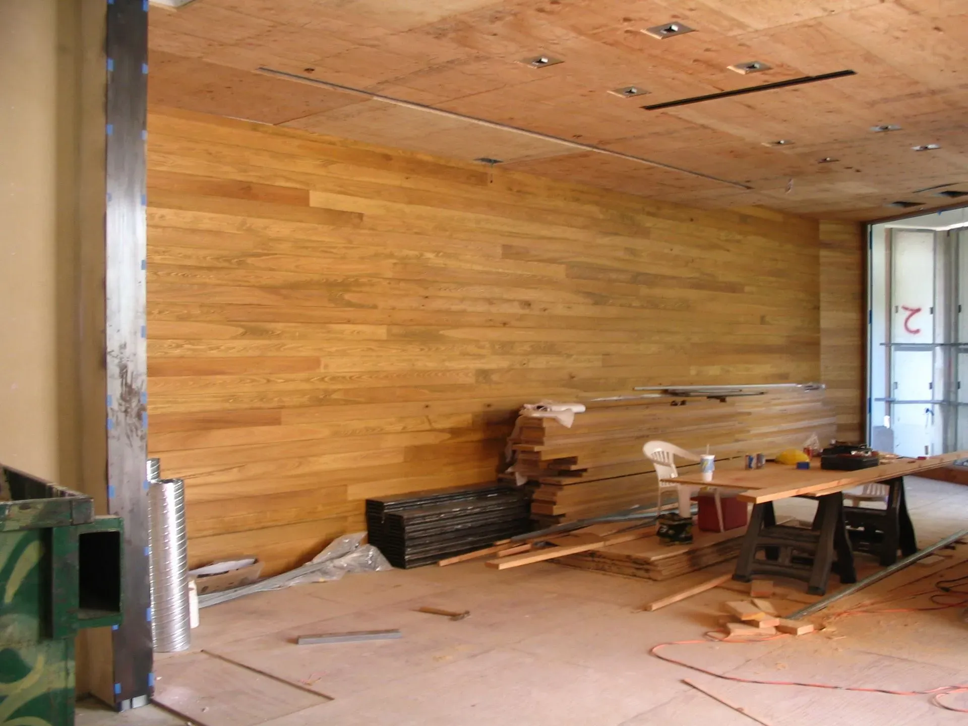 Partially finished room with wood-paneled walls, exposed ceiling, and construction materials scattered on the floor