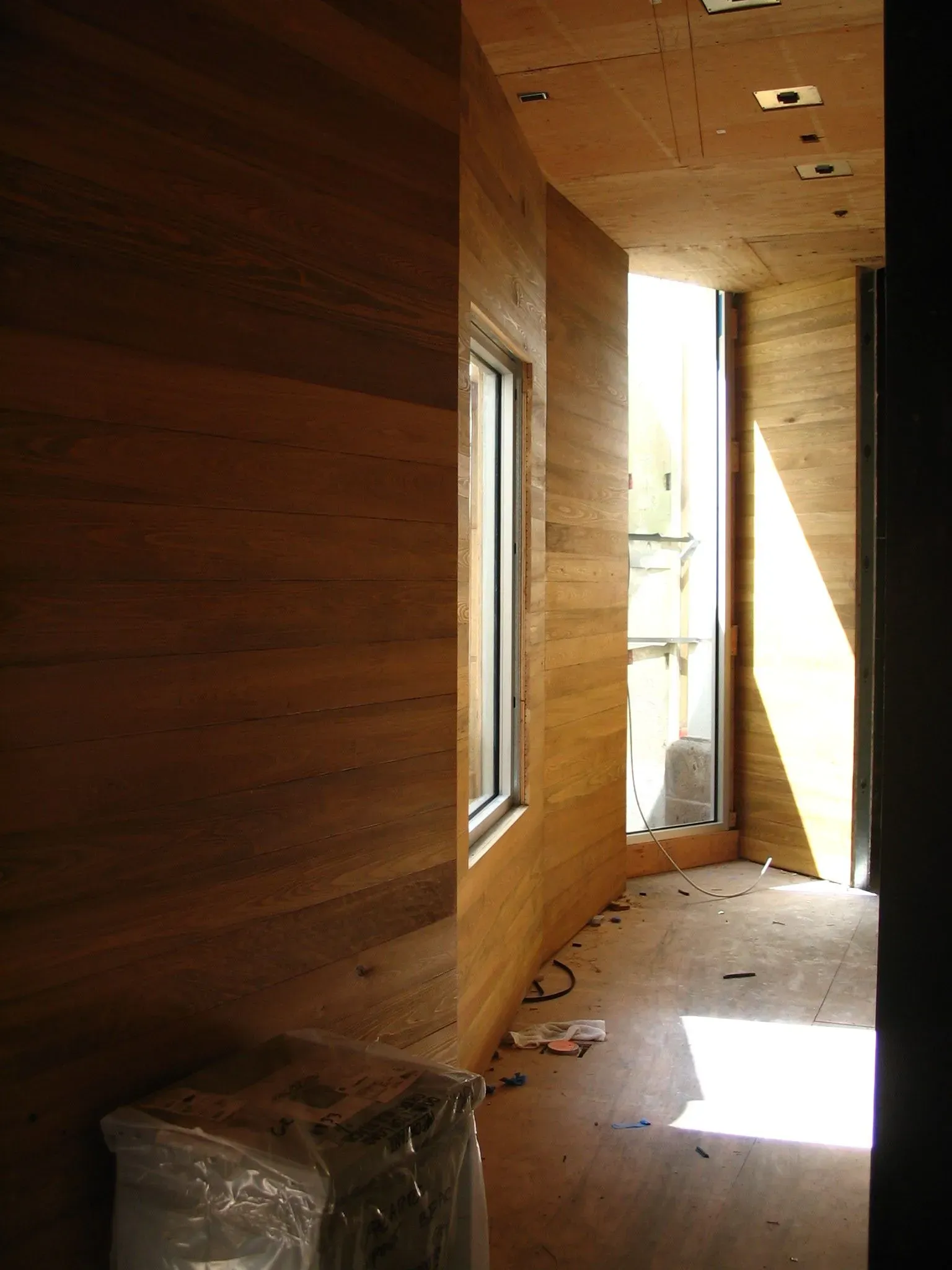 Narrow unfinished wooden hallway with window light and debris on the floor