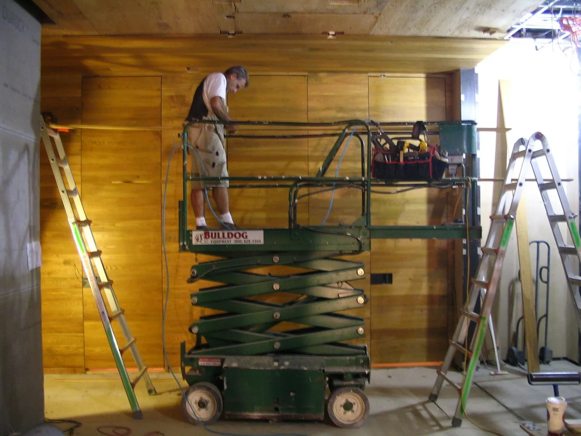 Worker on a scissor lift installing wood paneling inside a room
