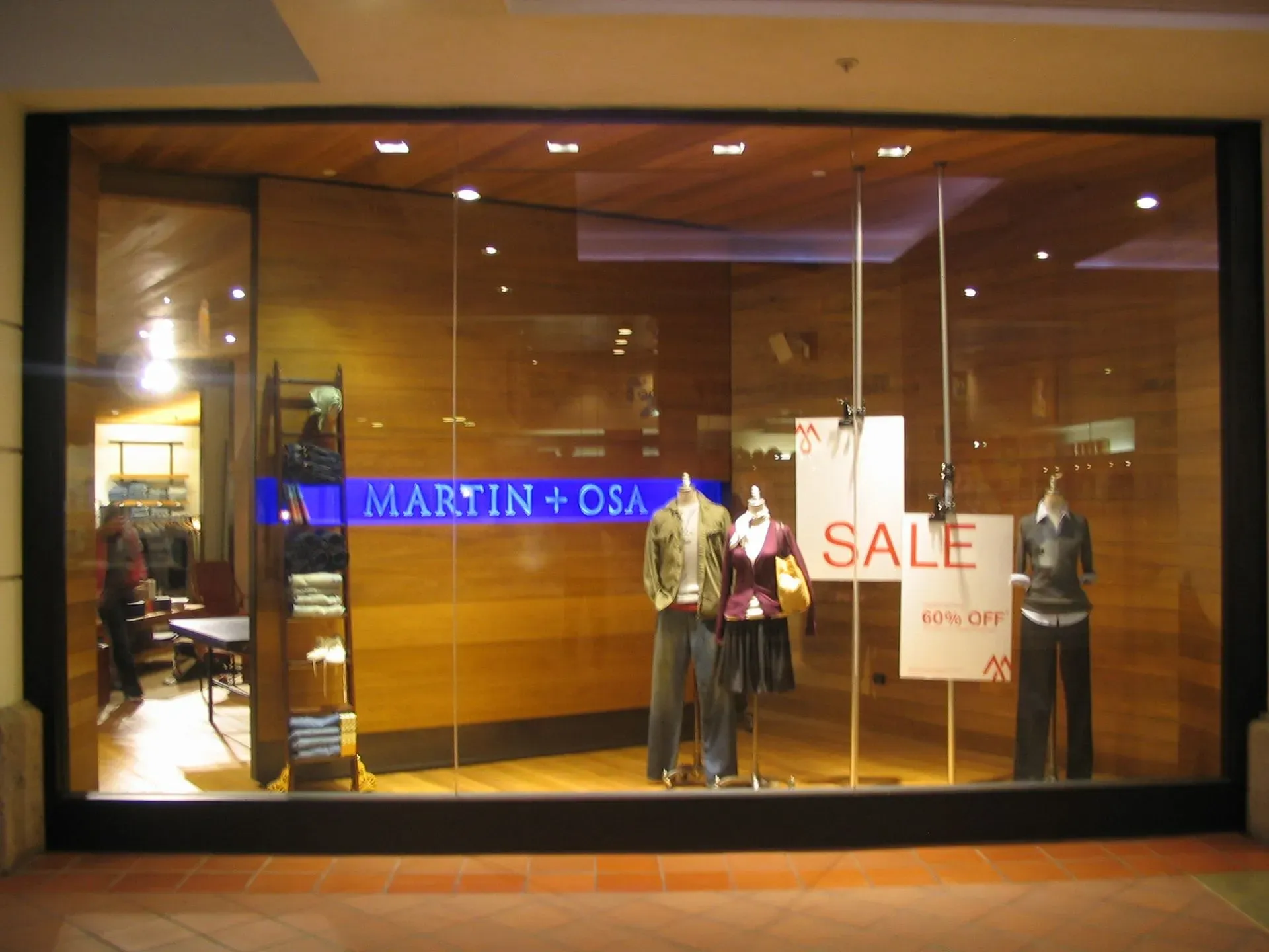 Storefront window display with mannequins and a large SALE sign at night