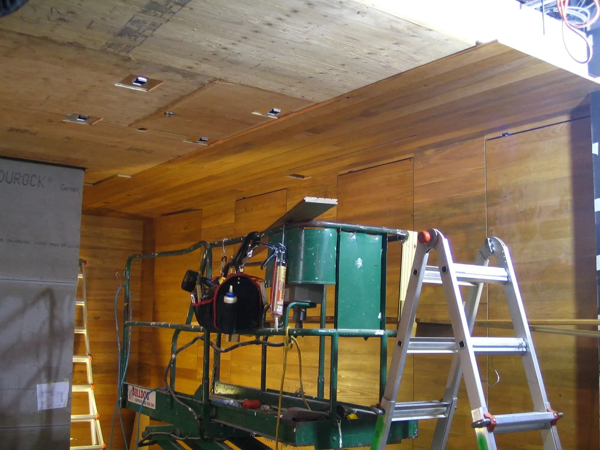 Scaffolding, ladders, and equipment inside a wood-paneled room under construction