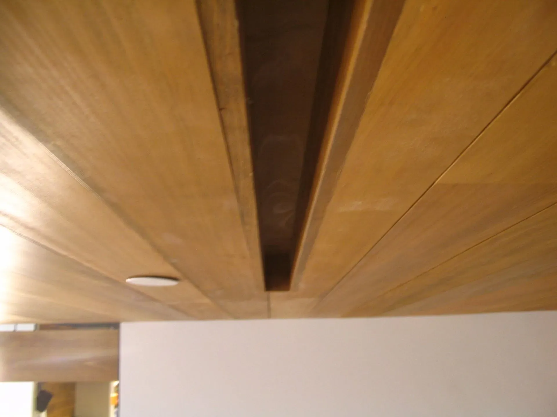 Wooden ceiling with long recessed light trough above a white wall