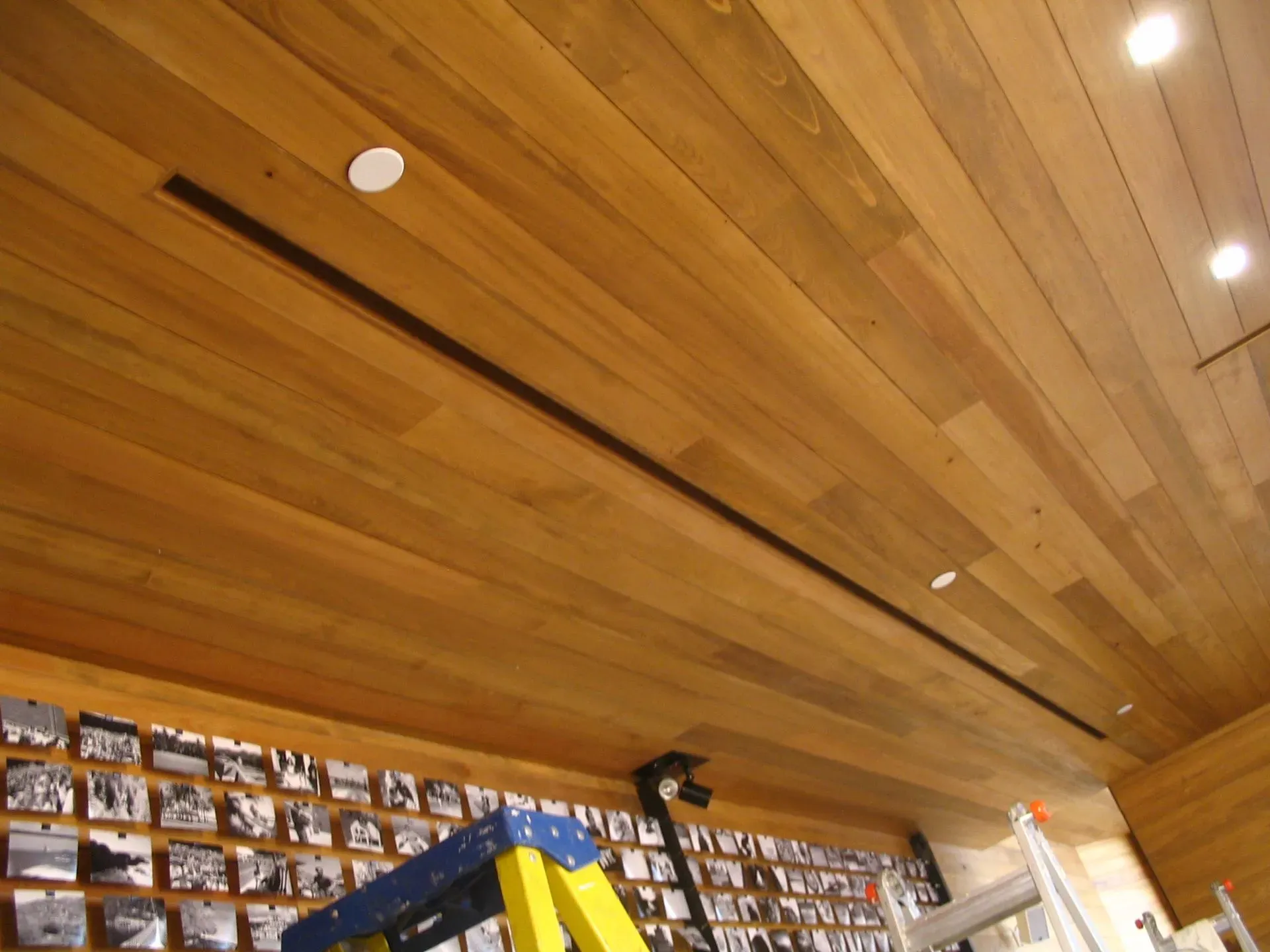 Wooden slat ceiling with recessed lights above rows of hanging photo displays in a shop or gallery