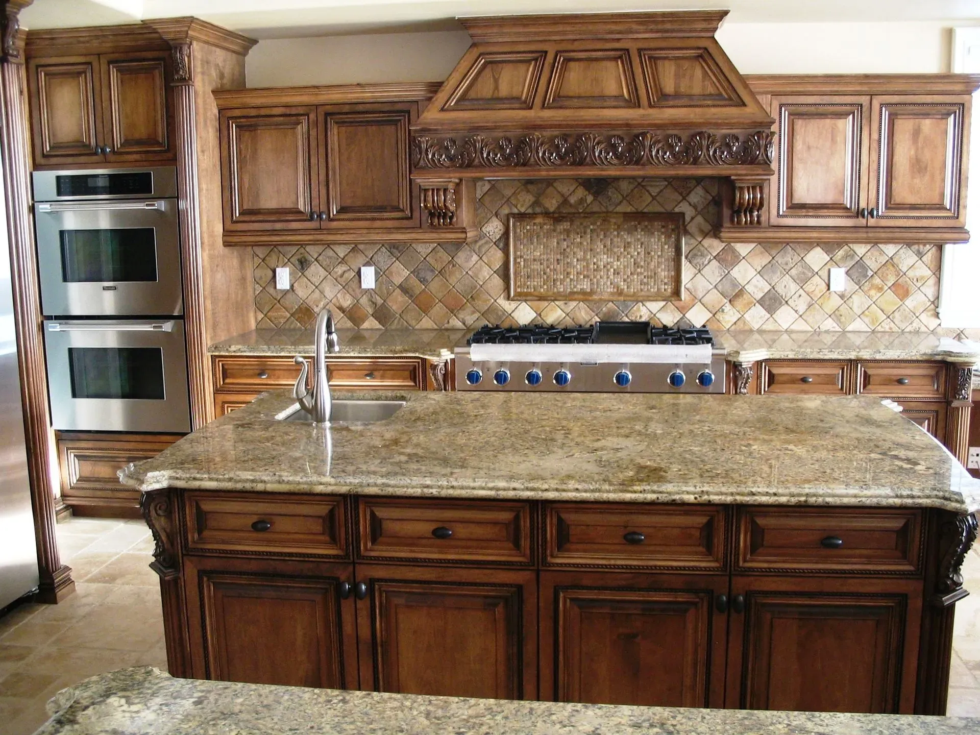 Wooden kitchen with granite island, built-in stainless oven, and ornate range hood