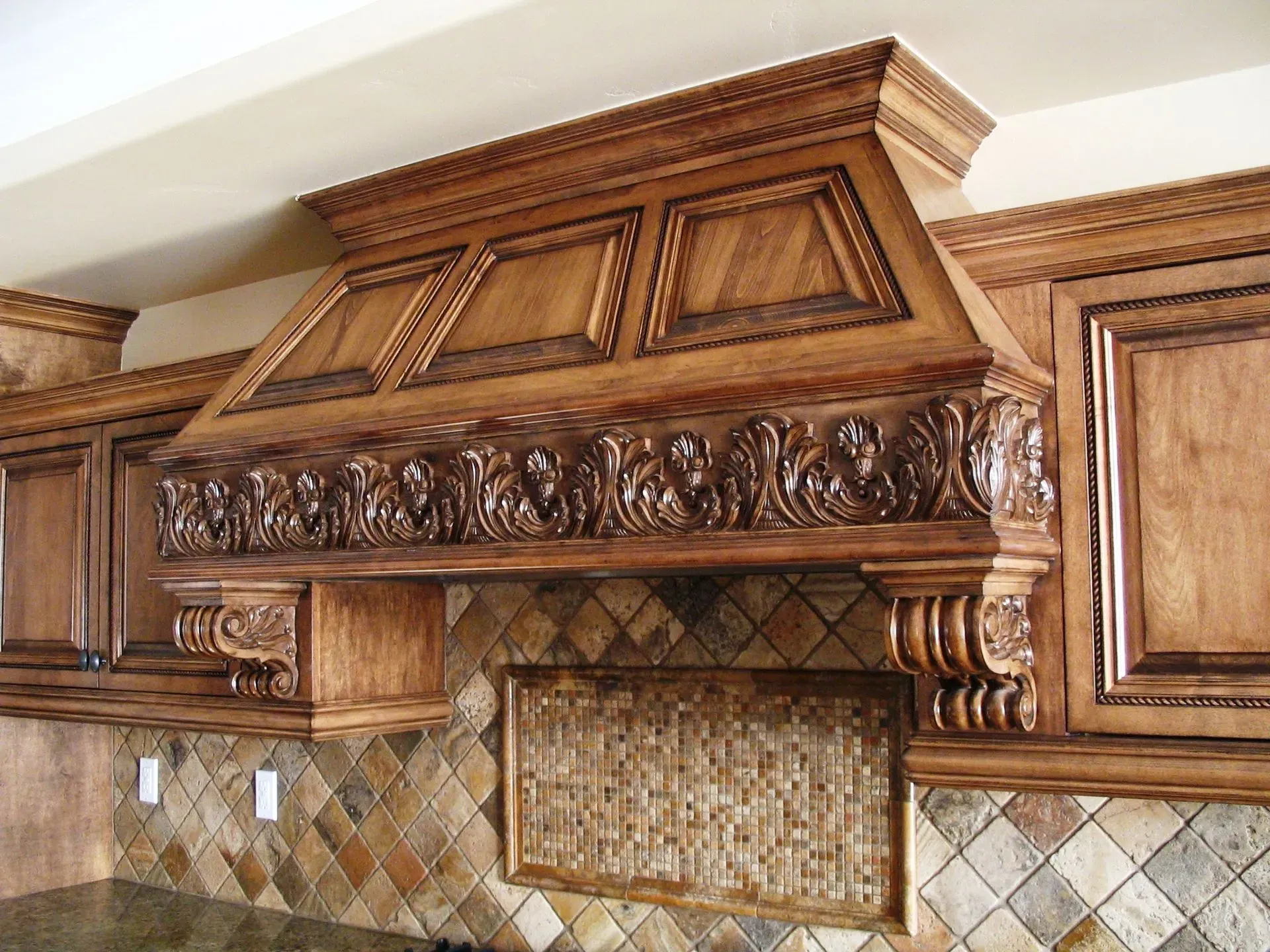 Ornate carved wooden kitchen range hood above a tiled backsplash and cooktop