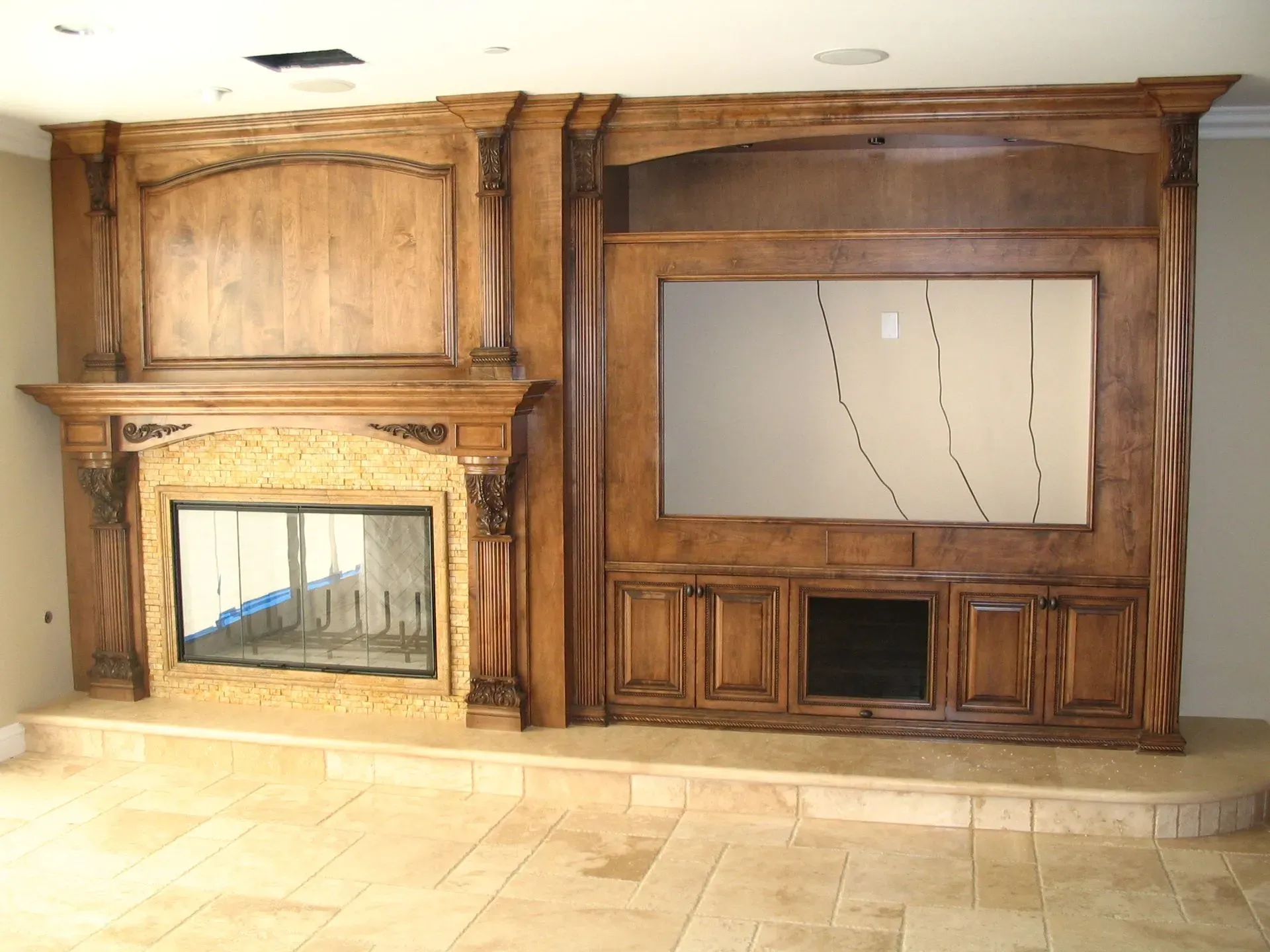 Wood-paneled living room wall with fireplace, built-in cabinets, and a large TV cutout above a small inset firebox