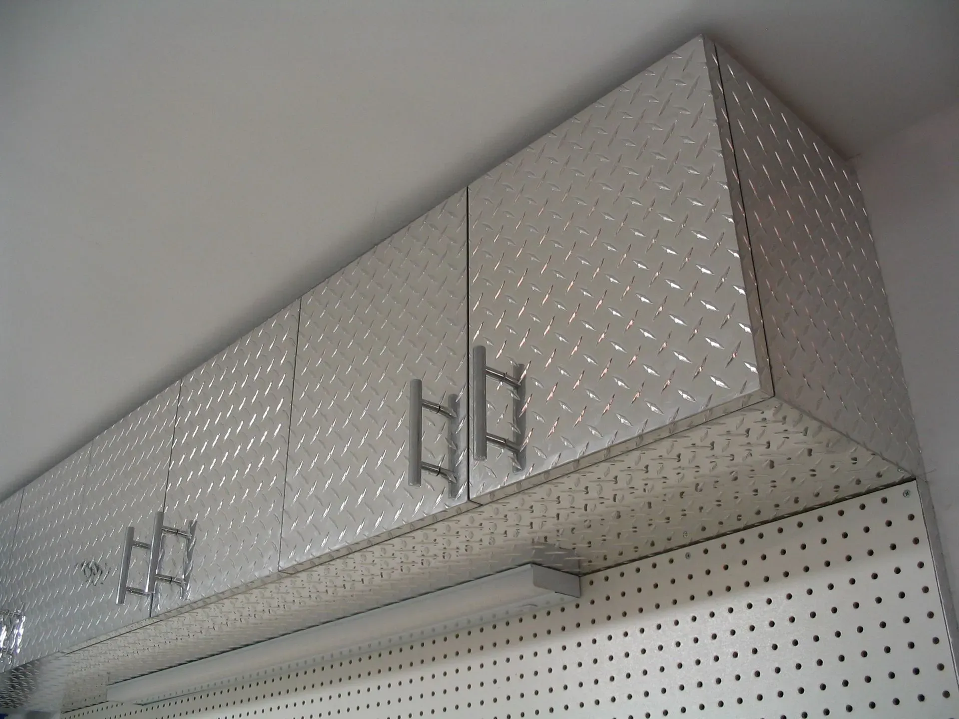 Silver diamond-plate metal cabinets mounted high on a wall above a pegboard shelf