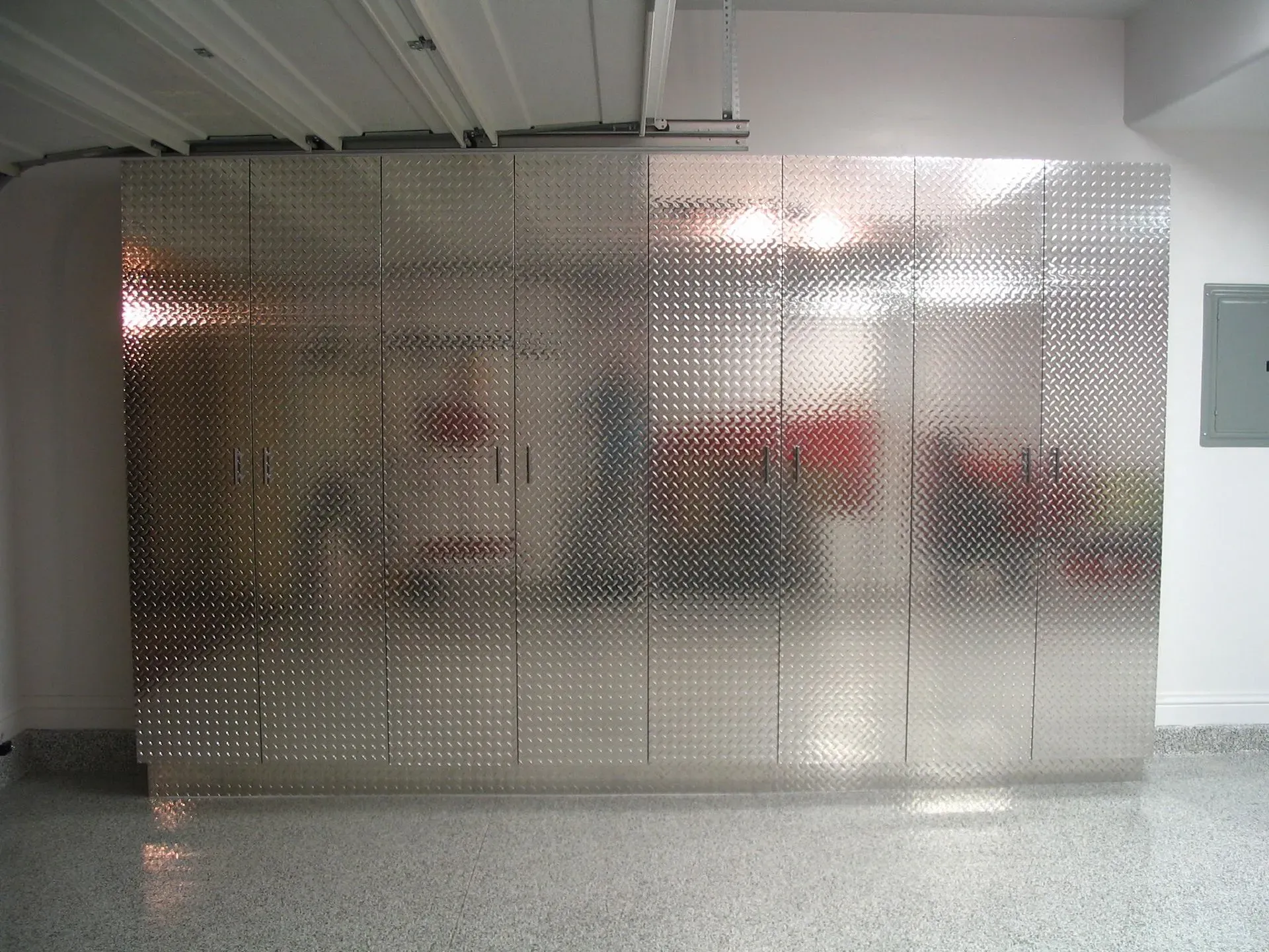 Metallic reflective wall panels in an indoor space with a concrete floor and ceiling pipes.
