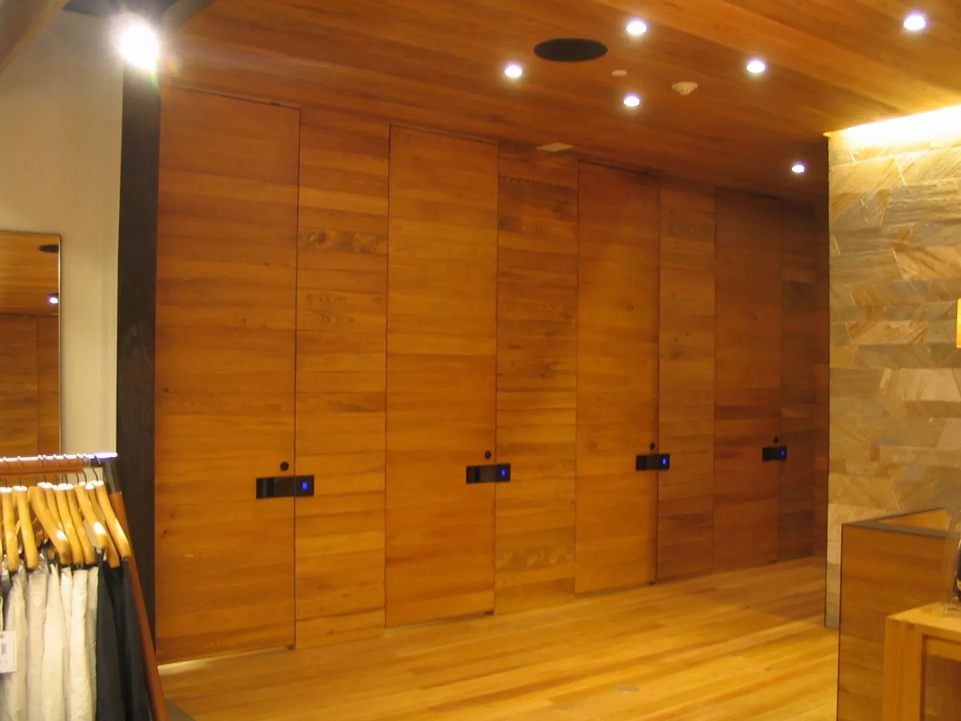 Wood-paneled retail fitting room area with mirrors, hanging clothes, and warm ceiling lights