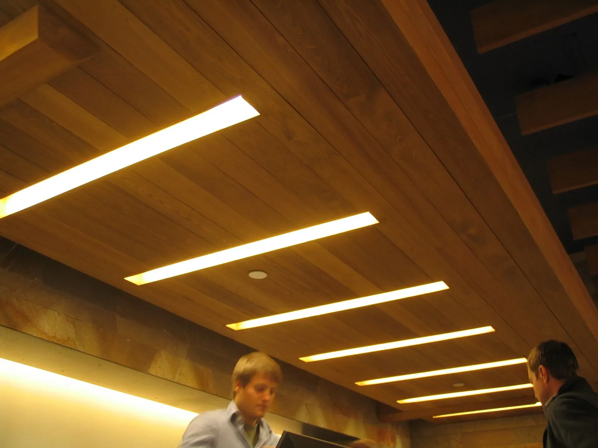 Two people in a wood-paneled hall under bright ceiling lights