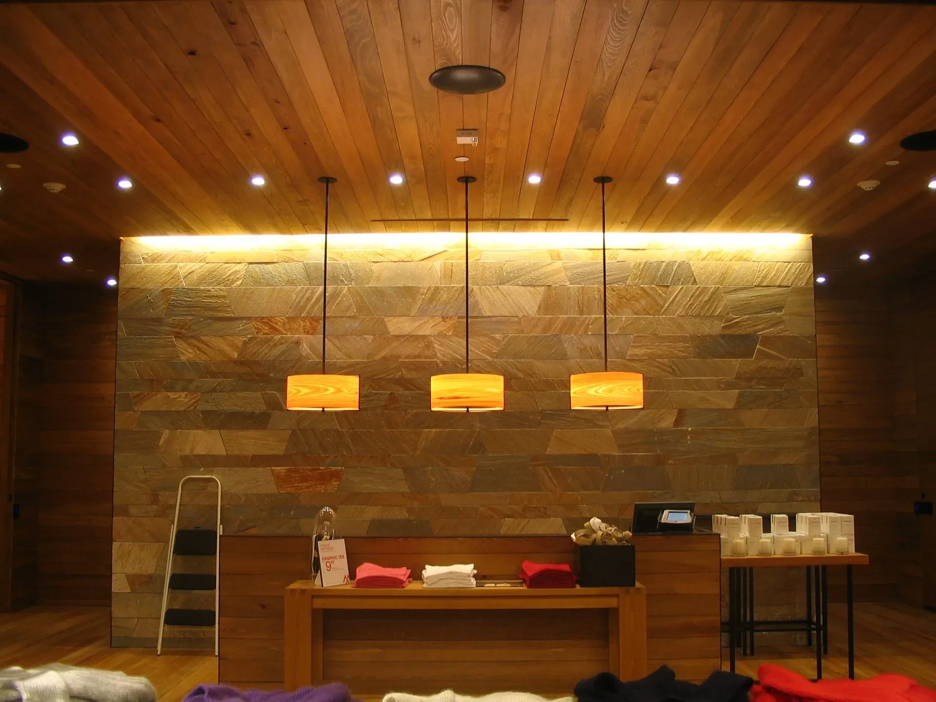 Wood-paneled restaurant counter with hanging pendant lights and shelves of cups against a stone wall