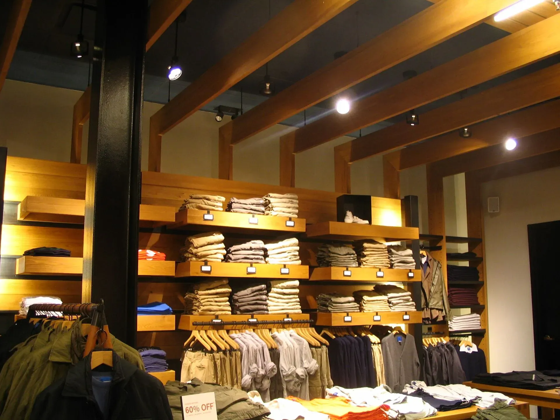 Clothing store interior with folded shirts on wooden shelves and hanging jackets under warm lights