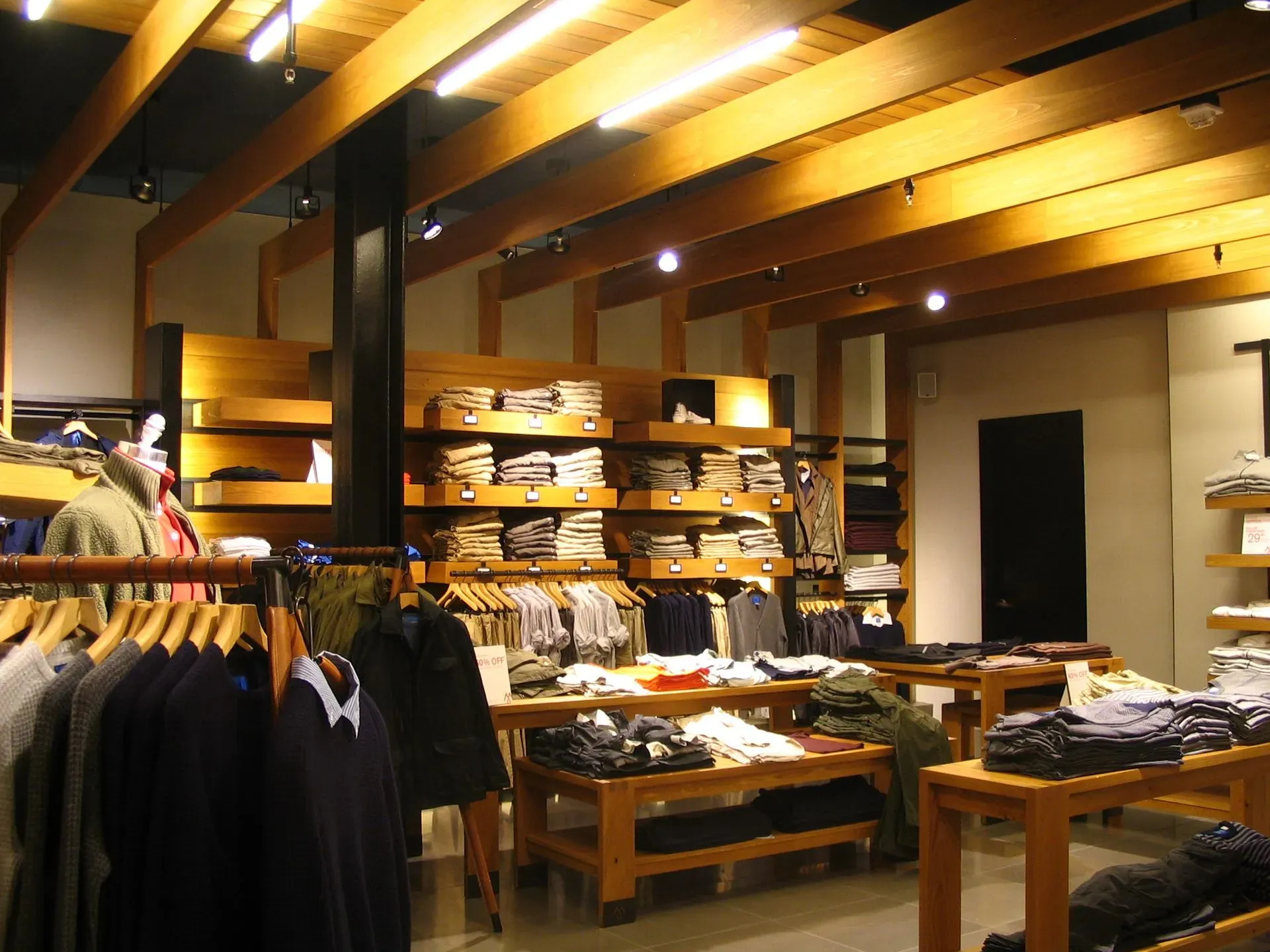 Clothing store interior with wooden shelves, folded sweaters, and hanging jackets under warm lighting