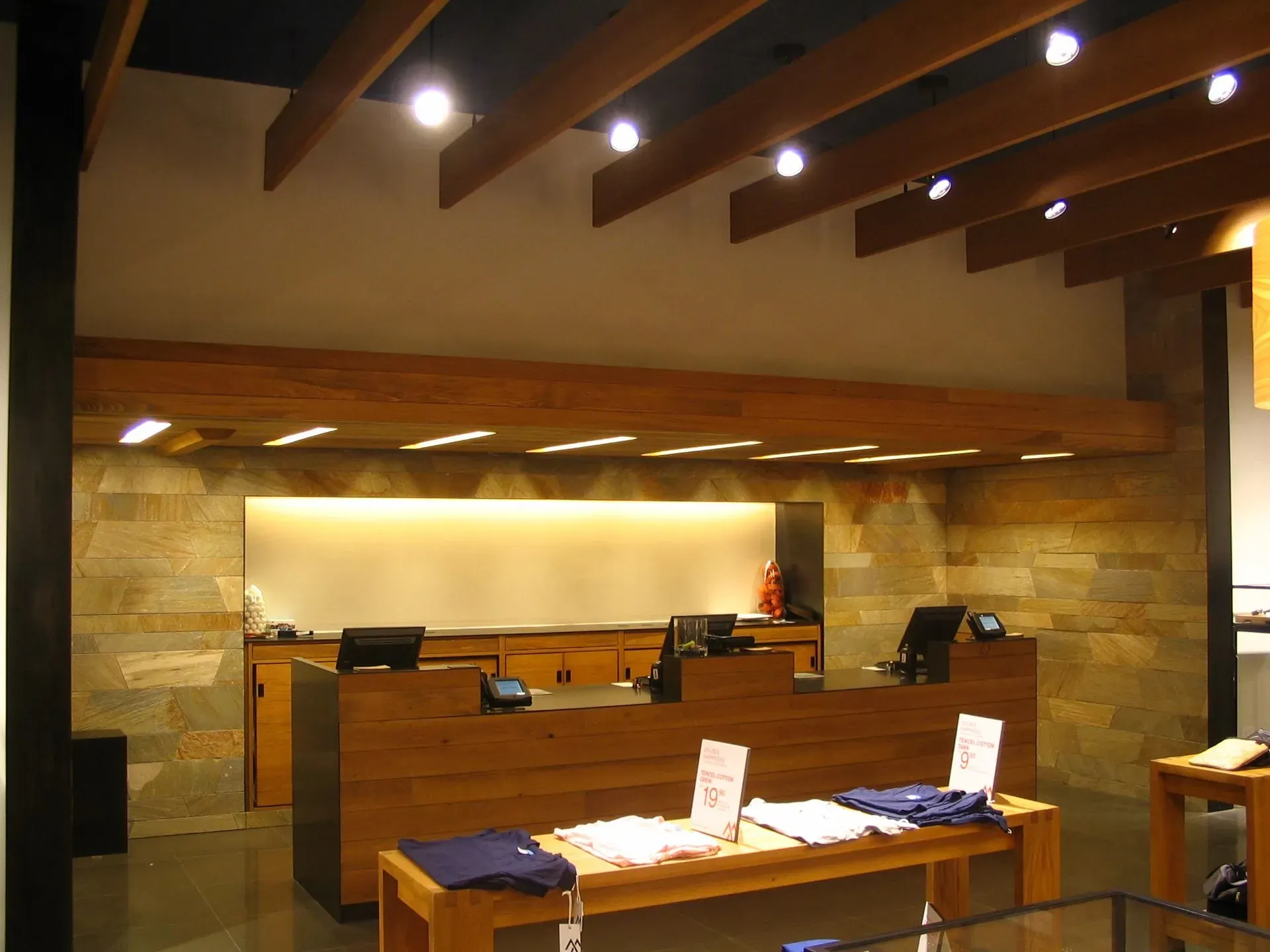 Modern lobby with wood-beam ceiling, stone walls, and reception desks under warm lighting