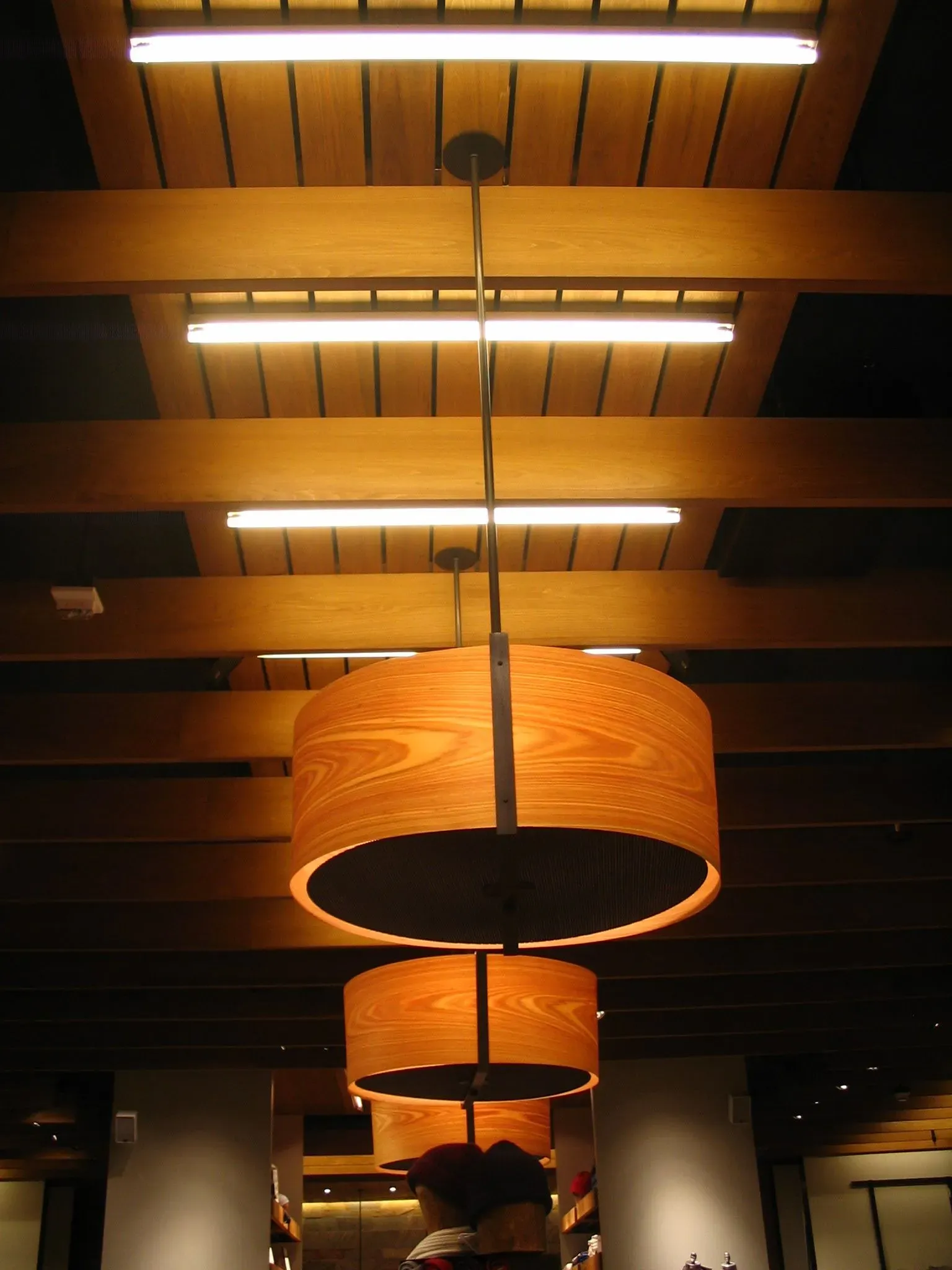 Rows of warm orange hanging lamps in a wood-paneled interior ceiling