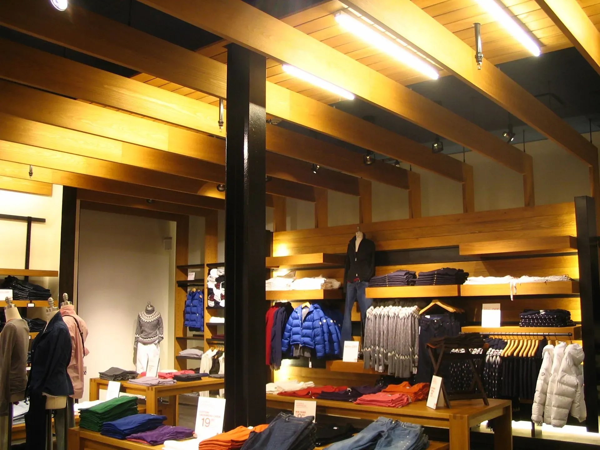 Clothing store interior with wooden beams, shelves, and racks of jackets and shirts under warm lighting