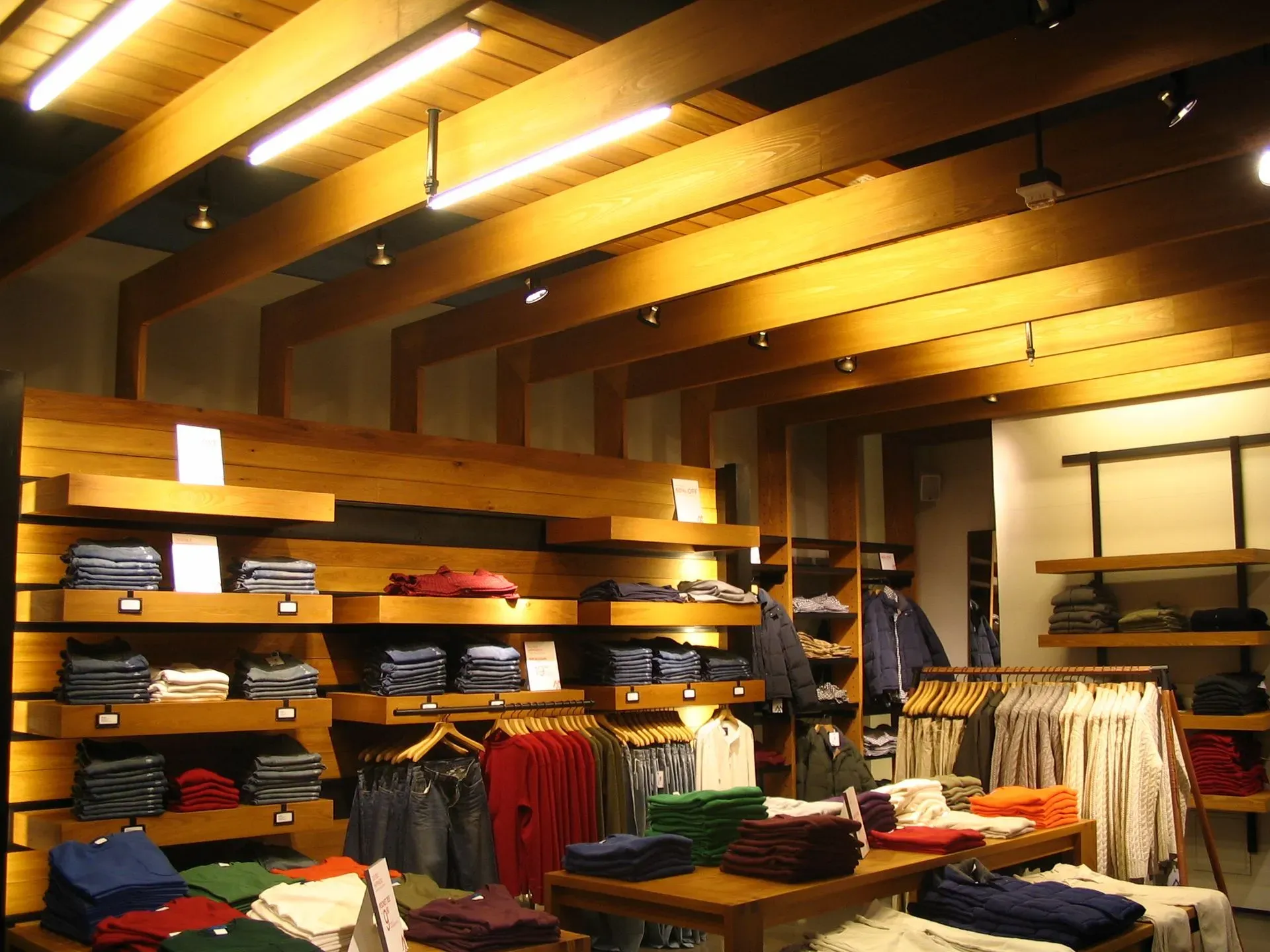 Clothing store interior with wooden shelves, folded shirts, and hanging garments under warm lighting